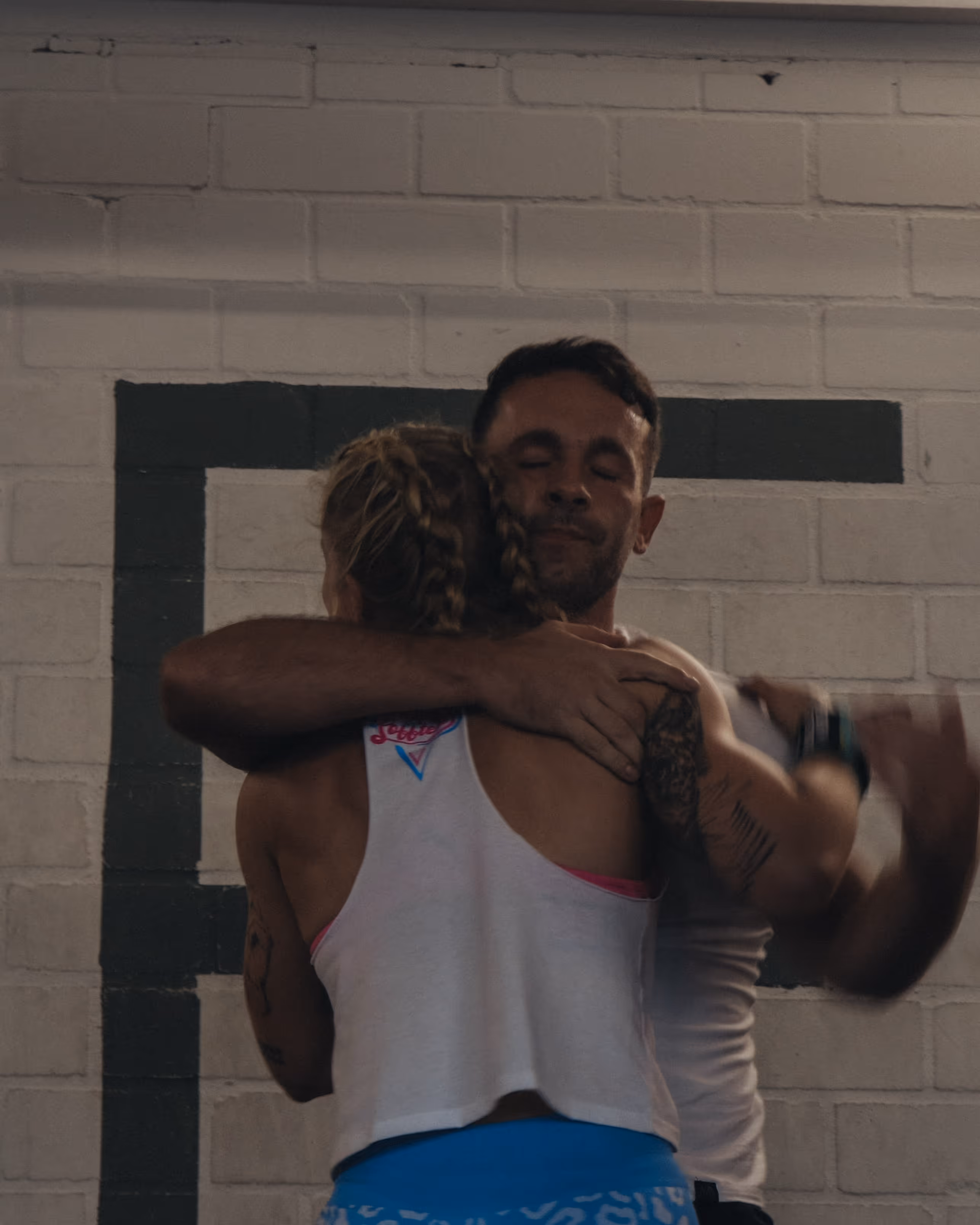 Ein Mann und eine Frau umarmen sich vor einer weißen Ziegelwand.