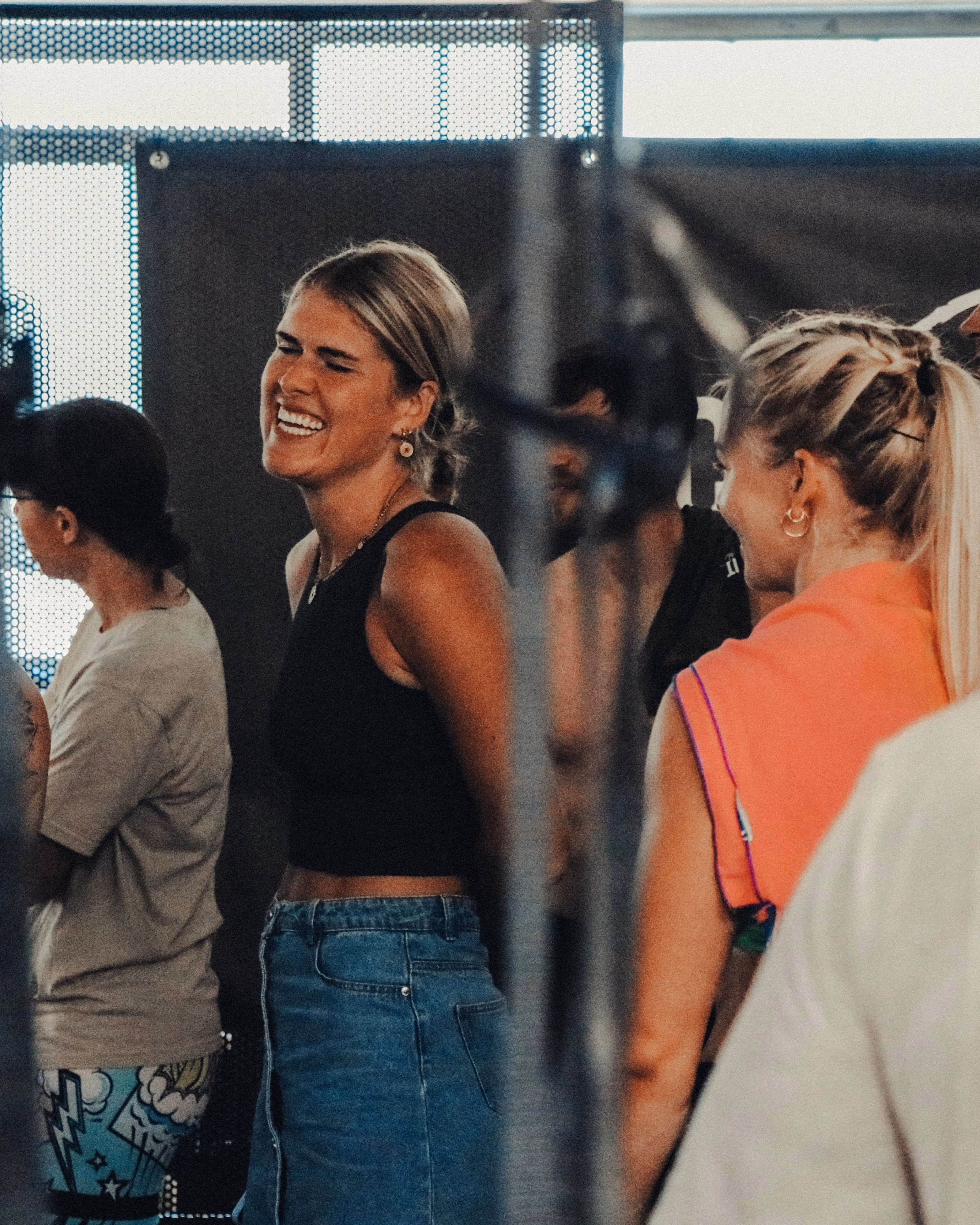 Eine lachende Frau mit schwarzem Top und Jeansrock steht in einer Gruppe von Menschen.