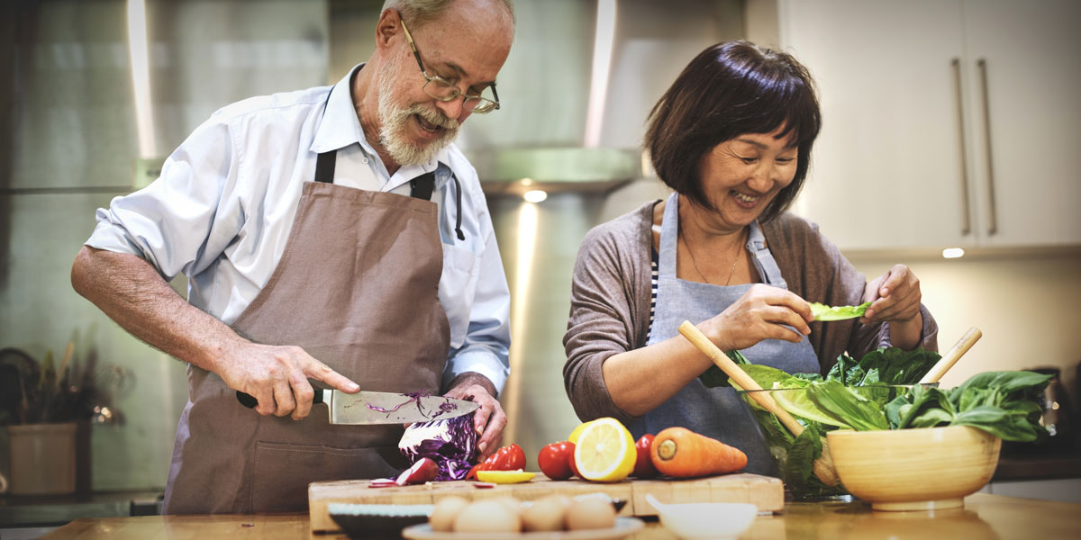 multi-ethic middle aged couple cooking together in their kitchen.