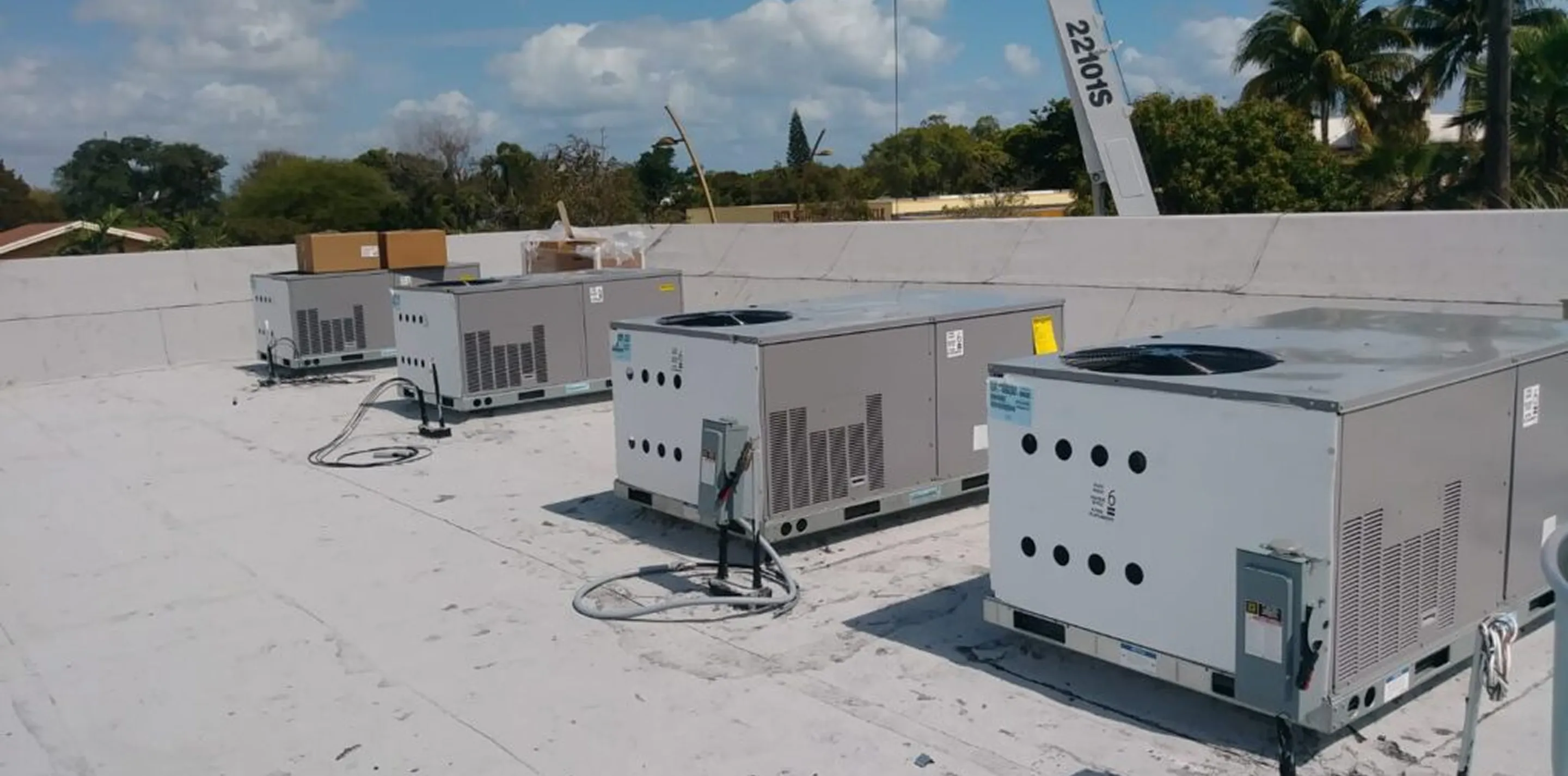 Three large HVAC units installed on a flat rooftop with a partly cloudy sky and trees in the background.
