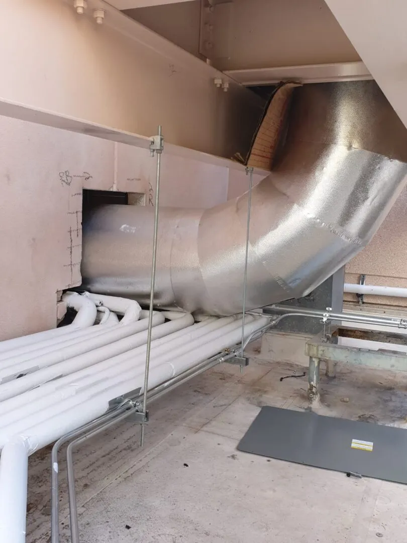 Large metallic industrial ductwork and white pipes in mechanical room
