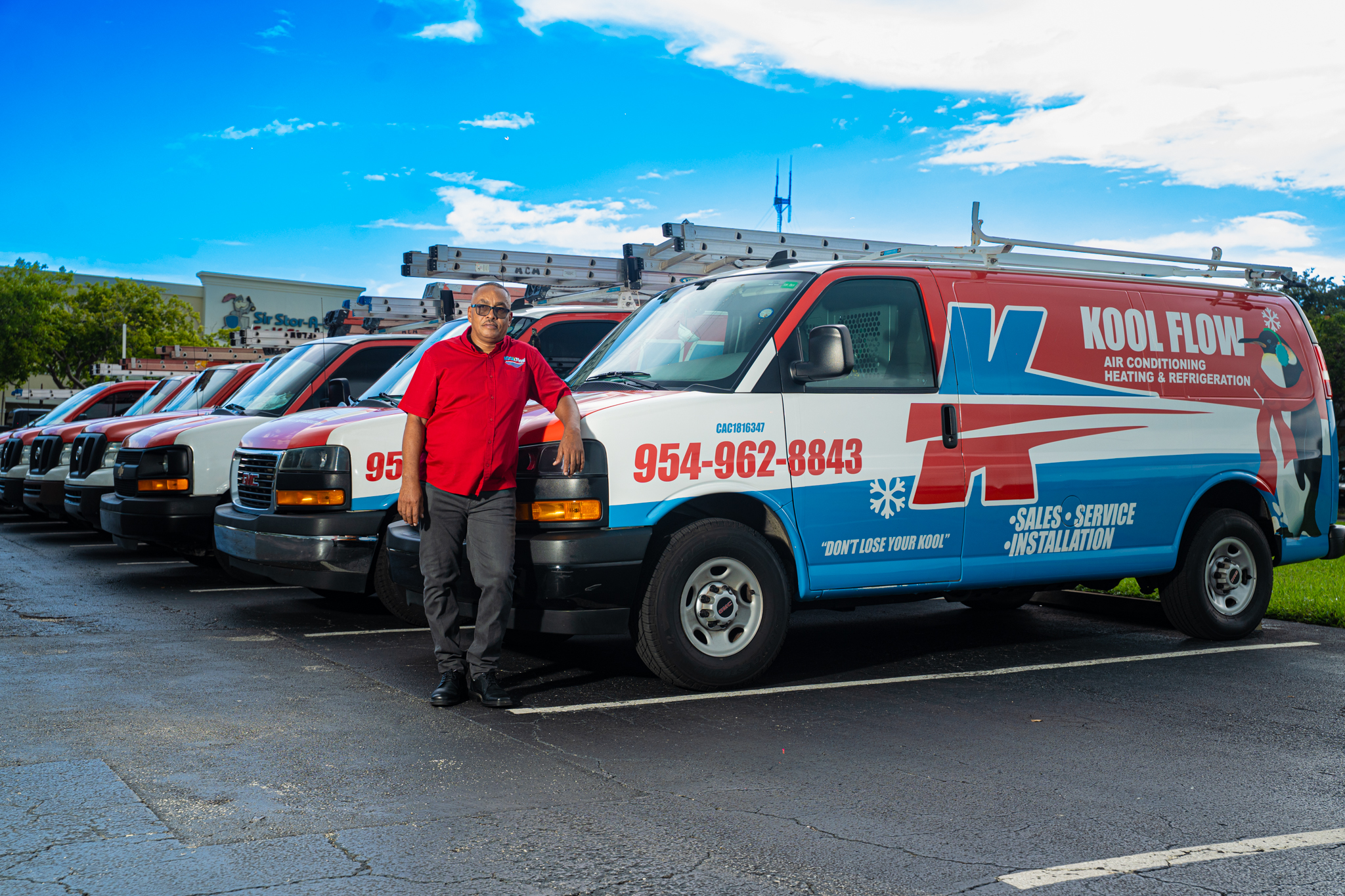 Man in red shirt leaning against a Kool Flow air conditioning and heating service van among a row of similar vans.