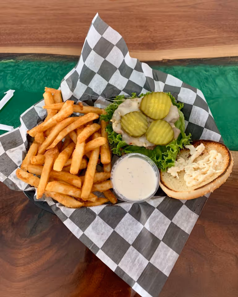 A burger with melted cheese, pickles, and lettuce on a bun beside golden fries and ranch dressing.