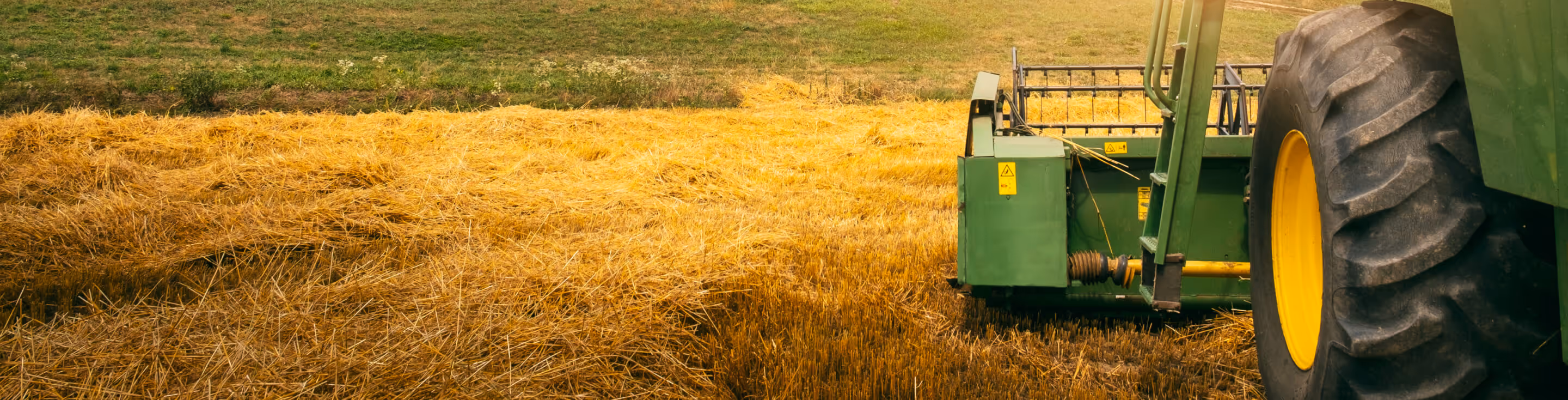 Close-up of a green tractor's large rear wheel and attached harvesting equipment working on a golden wheat field.