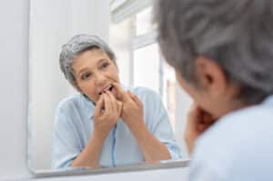 Senior woman flossing in mirror as part of her gum disease treatment plan