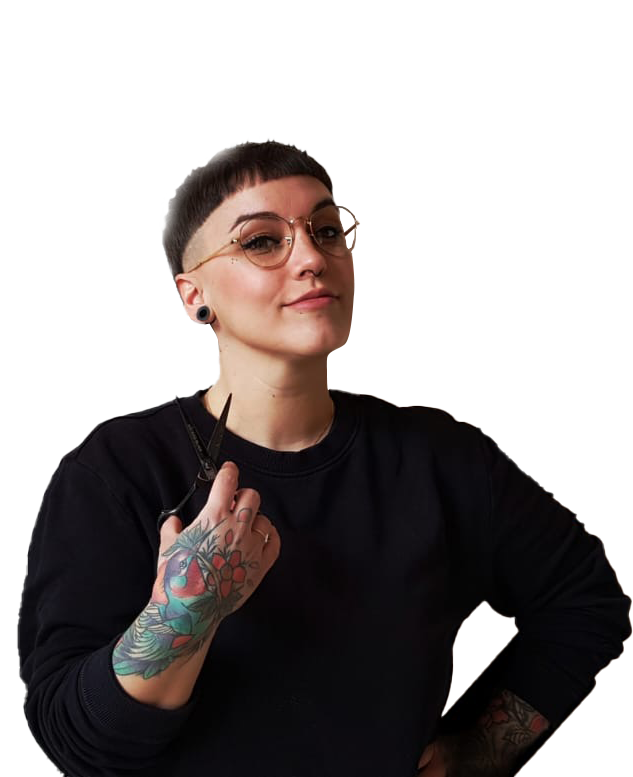 Person with short dark hair, glasses, and tattoos on their arm holding a pair of scissors, wearing a black shirt.