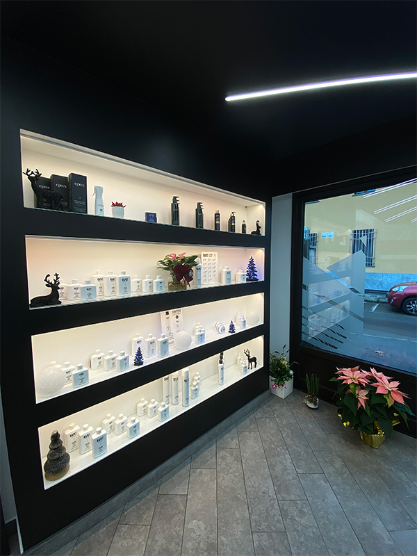 Modern display shelves with illuminated skincare and haircare products, decorated with small poinsettia plants and festive decorations near a glass door.