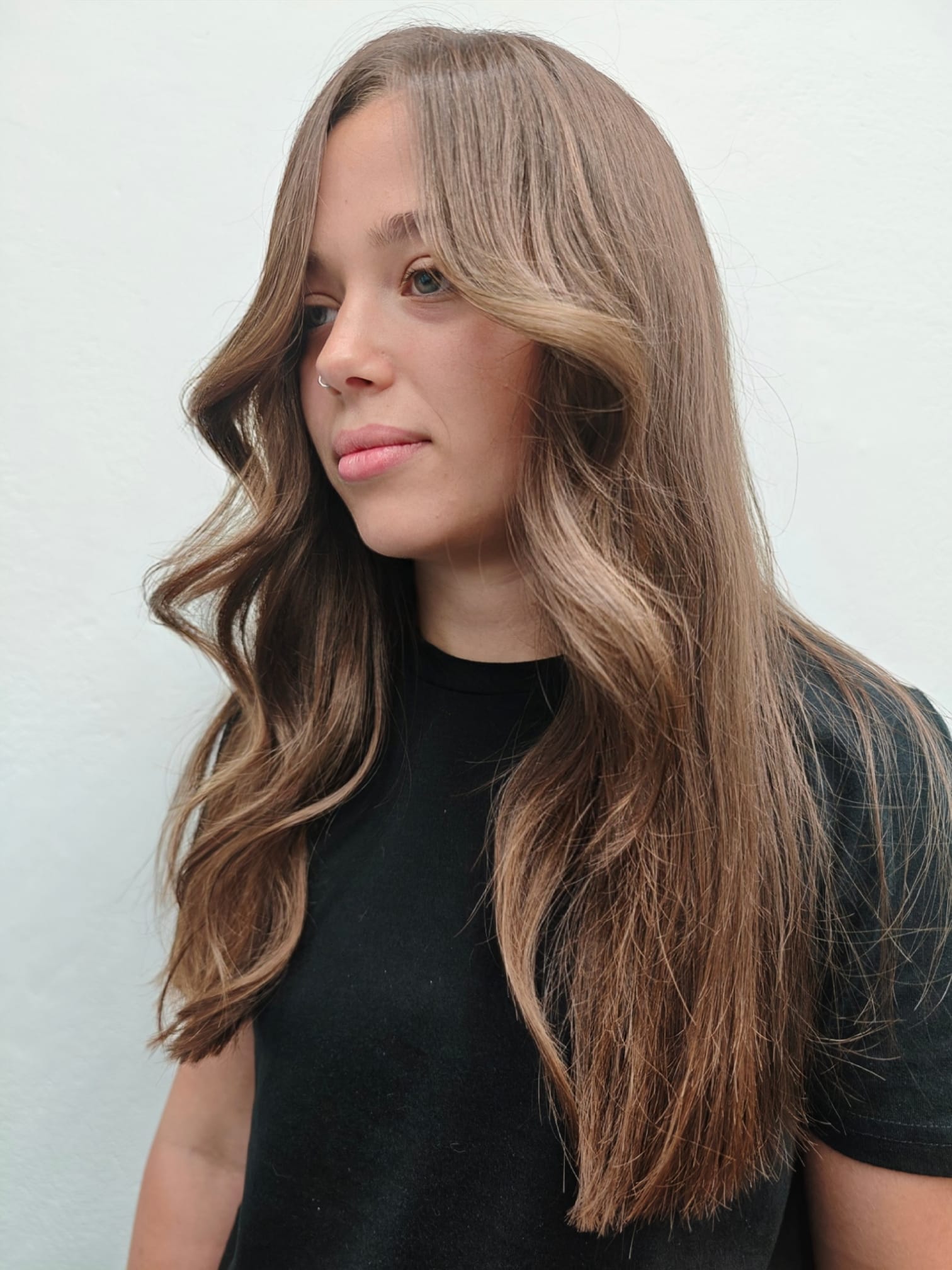 Side profile of a woman with long, dark wavy hair being styled by a tattooed hand against a plain white background.