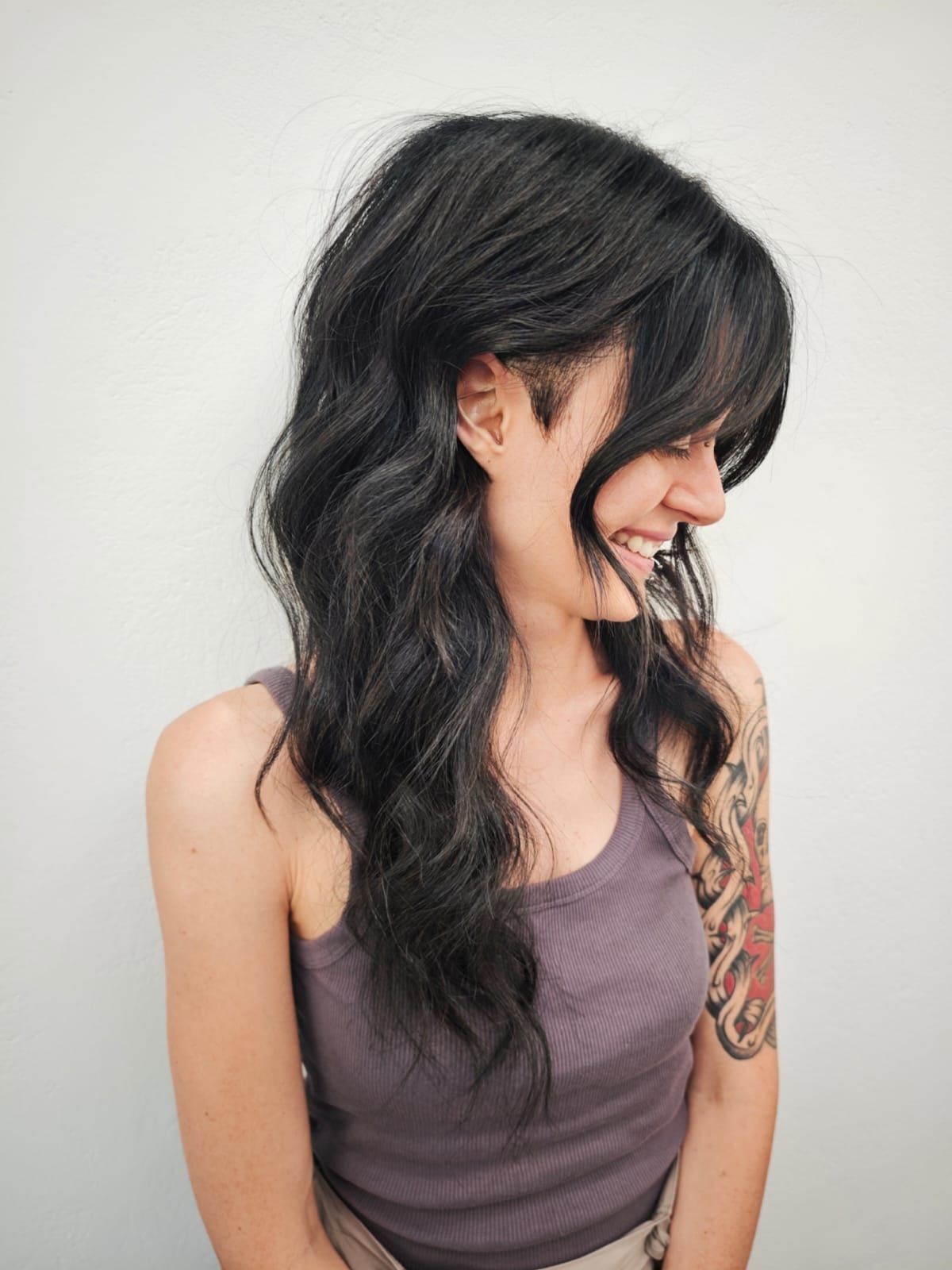 Long, wavy brown hair cascading down the back against a plain light gray wall.