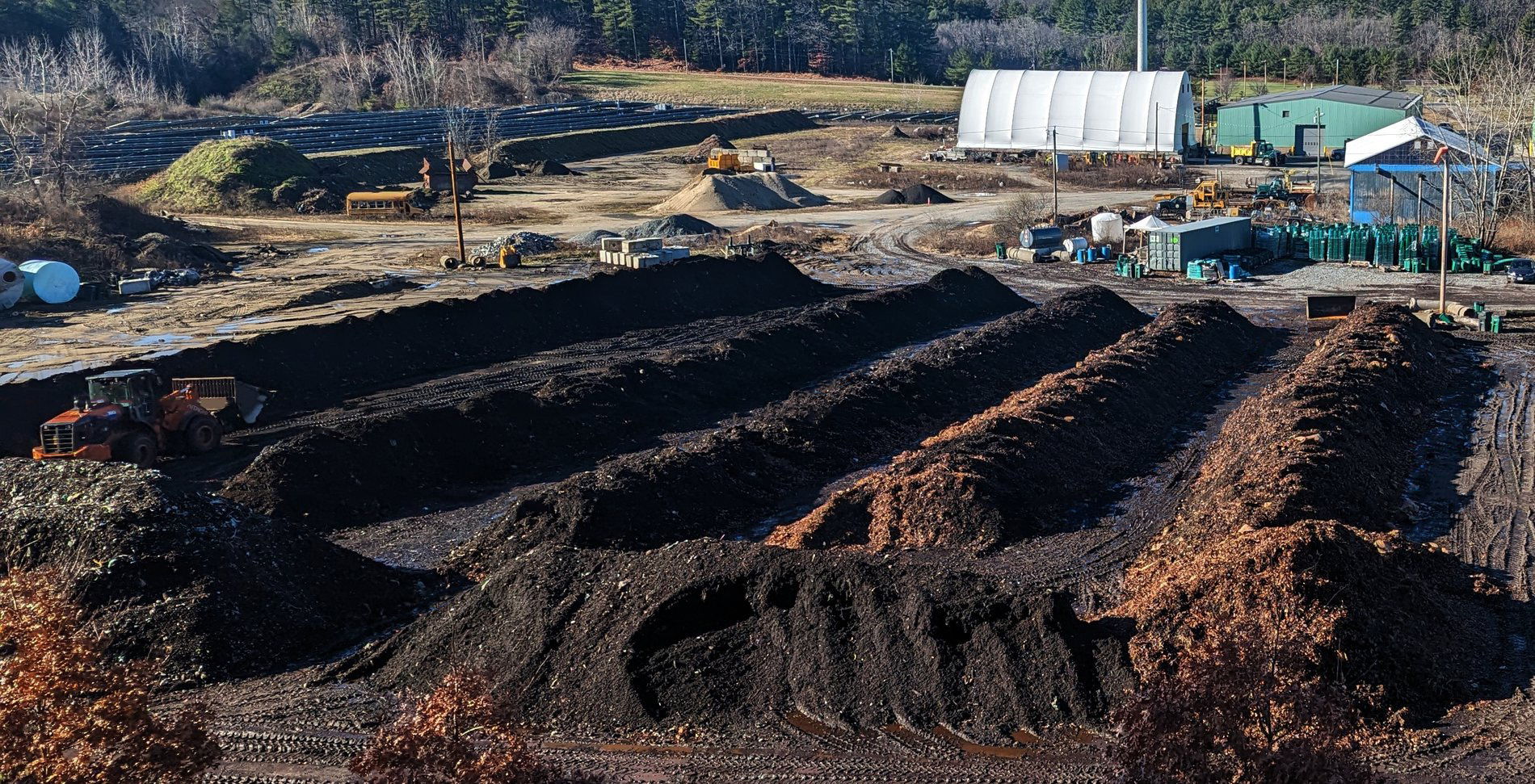 Aerial view of large composting windrows with heavy machinery at a recycling or waste management facility.