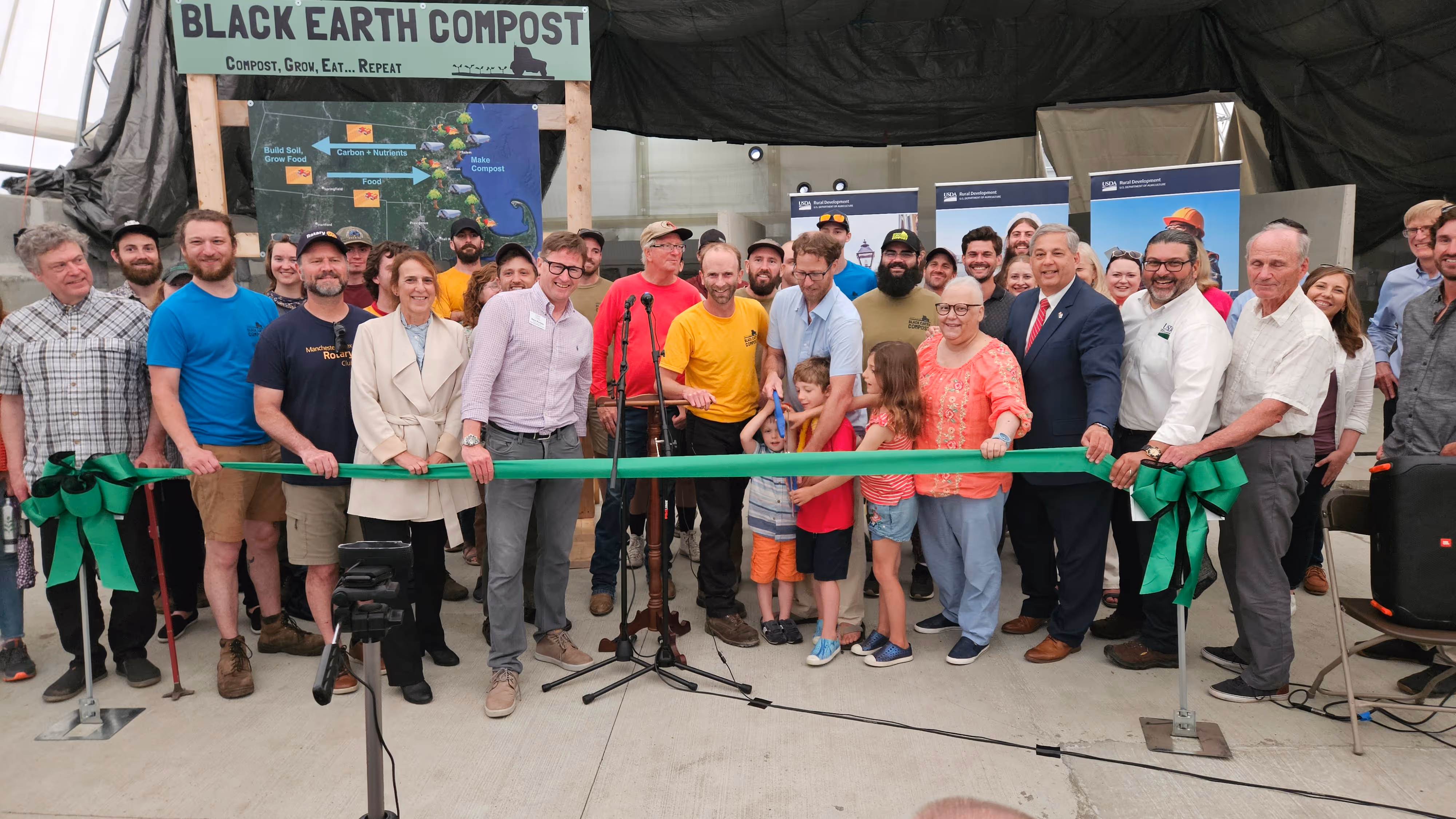 Group of people, including children and adults, gathered for a ribbon-cutting ceremony at Black Earth Compost.