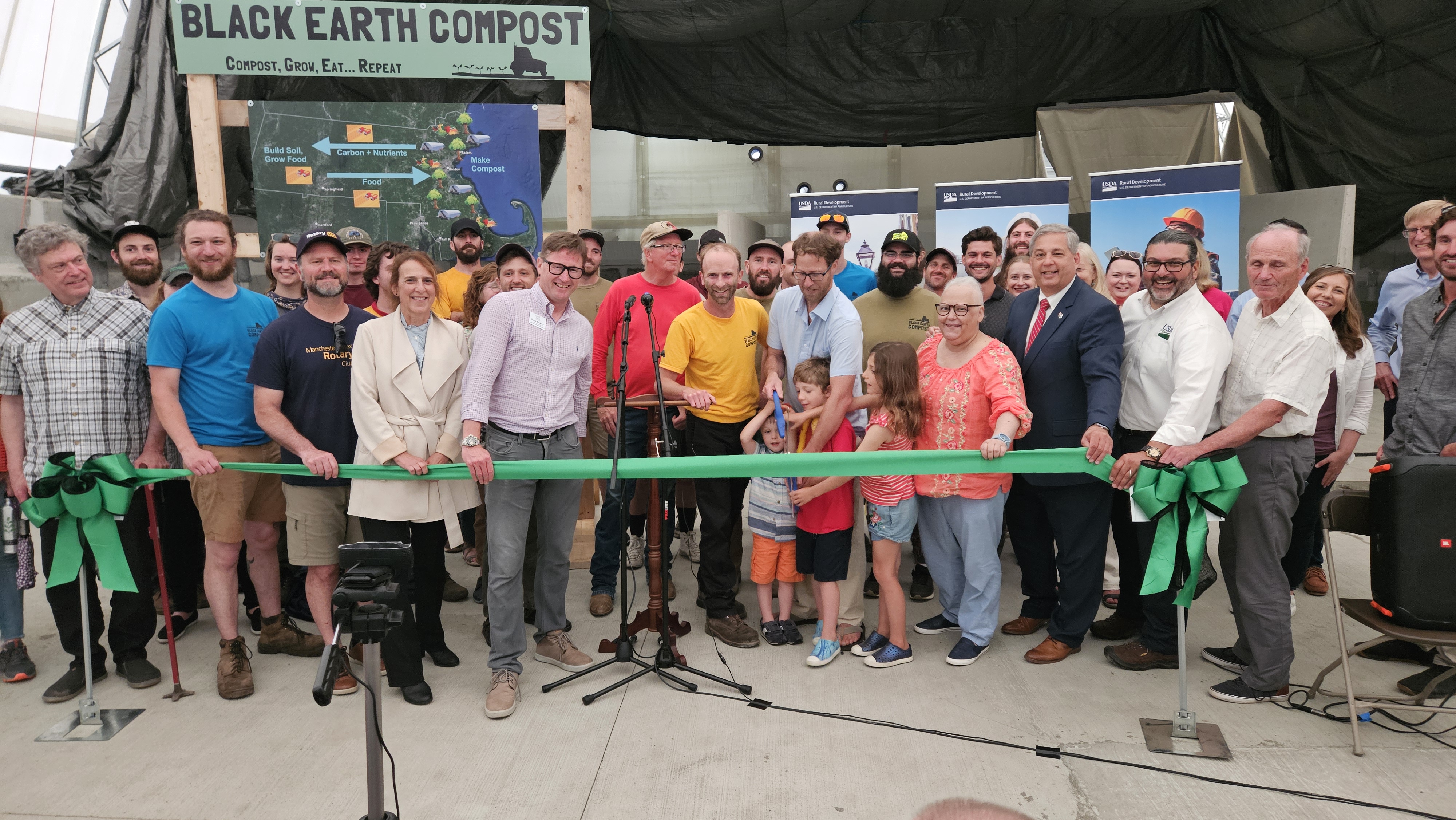 Group of people, including children and adults, gathered for a ribbon-cutting ceremony at Black Earth Compost.