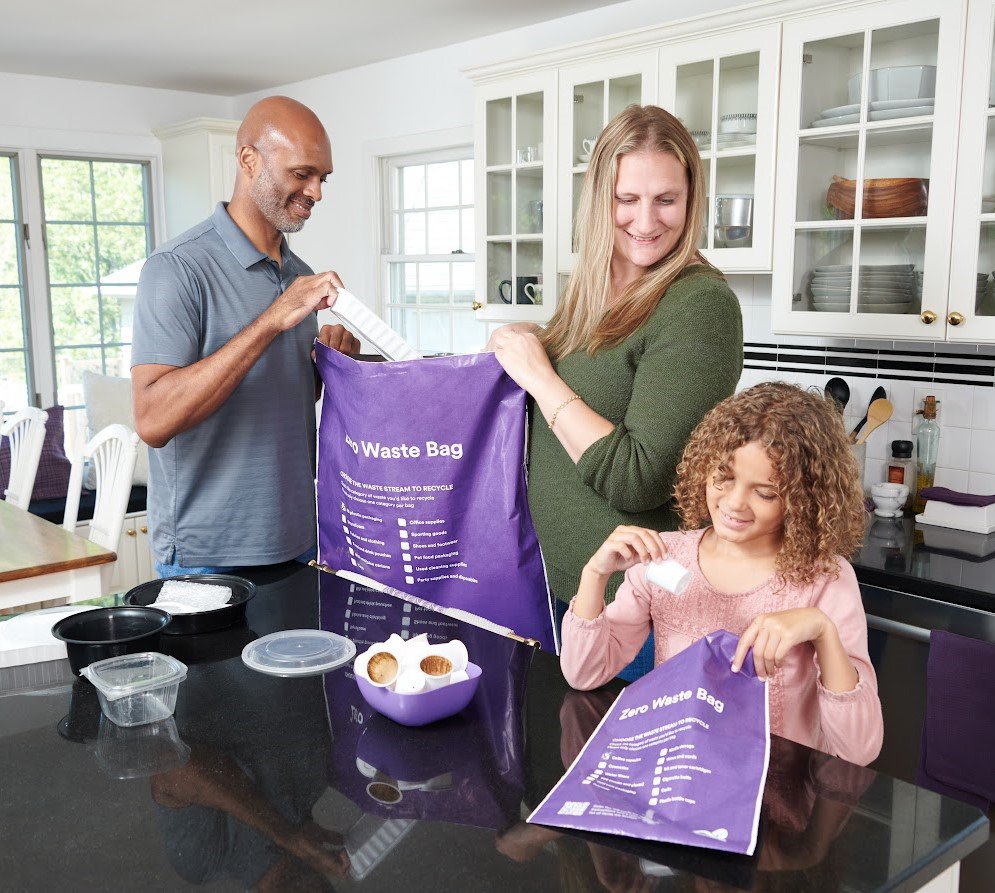 A family in a kitchen sorting recyclable items into purple bags labeled 'Zero Waste Bag' for recycling.