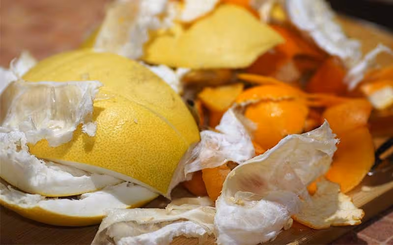 Close-up of mixed citrus fruit peels including yellow grapefruit and orange tangerine on a wooden surface.