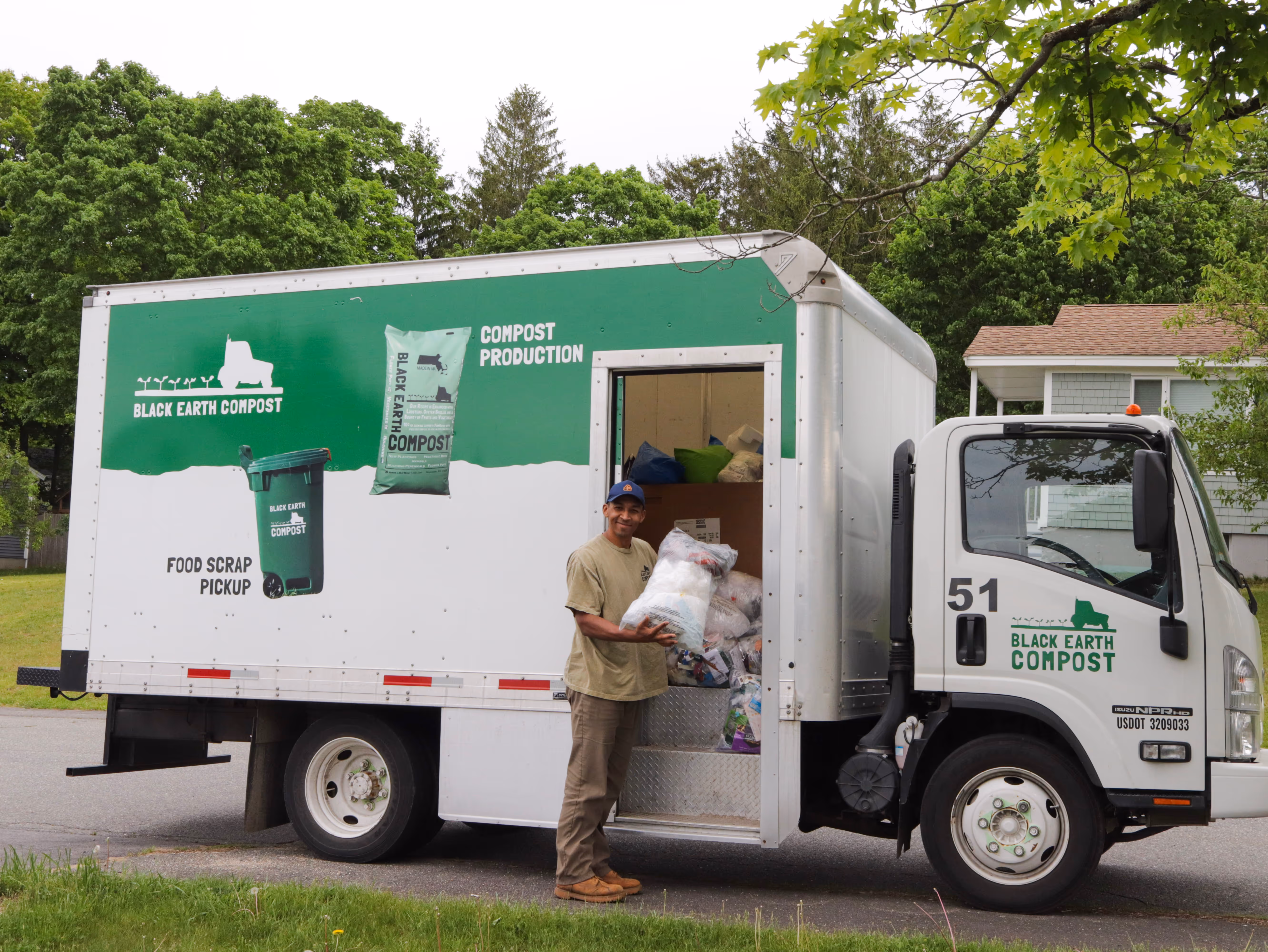 White and green waste management truck on a suburban street with message about handling food scraps, plastic, textiles, and electronics that make up half of household trash.