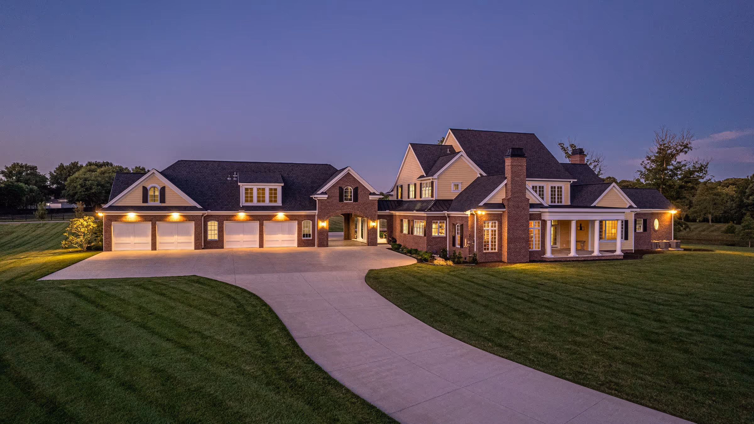 Large Traditional Southern house with multiple garages, well-lit windows, and a wide curved driveway at dusk.