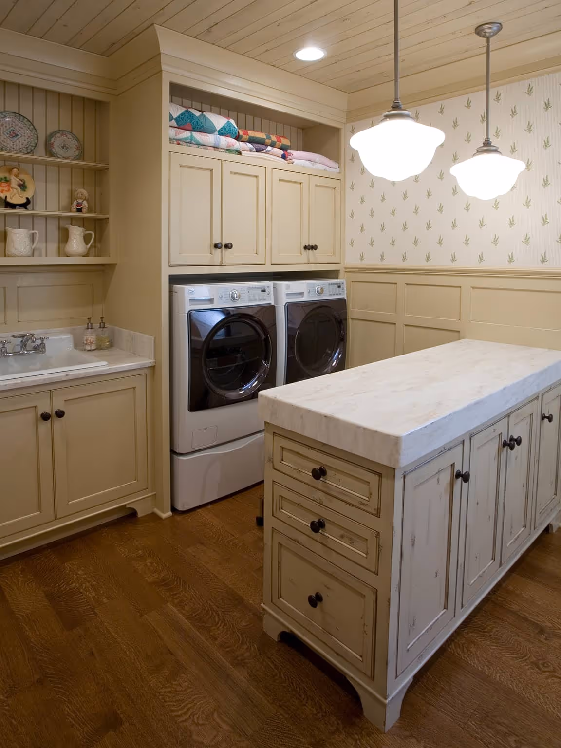 Laundry room with beige cabinets, front-loading washer and dryer, a marble-top island, and wooden flooring.