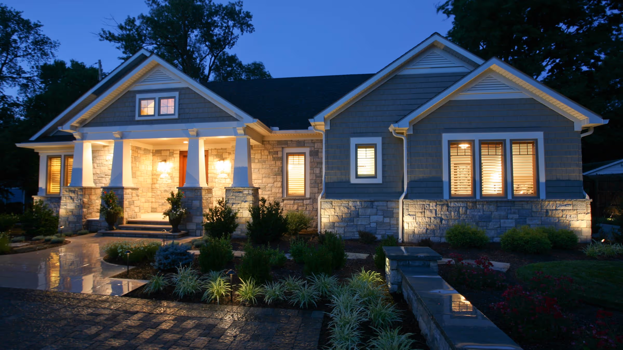 Well-lit Craftsman-style house with stone and blue siding exterior at dusk.
