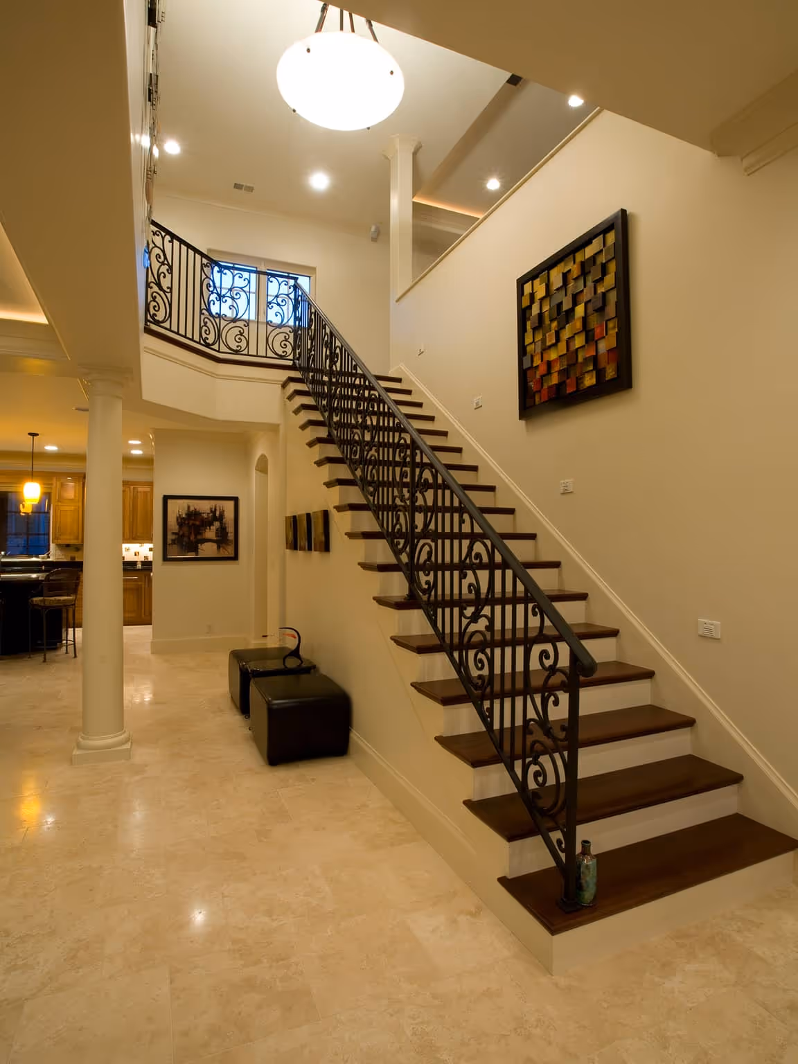Interior view of a home featuring a staircase with ornate black iron railing, beige marble flooring, and modern wall art.