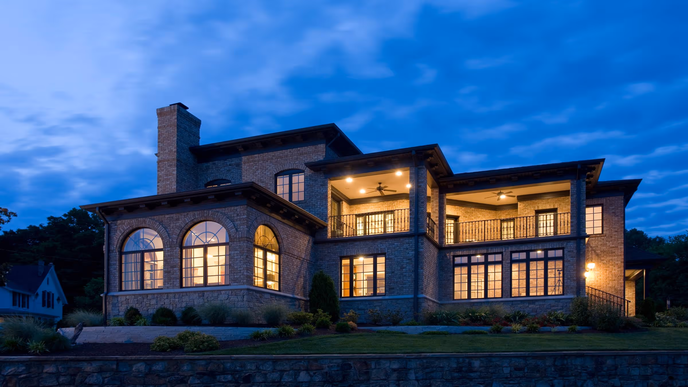 Large brick California Mediterranean style house illuminated at dusk with multiple windows and covered balconies.