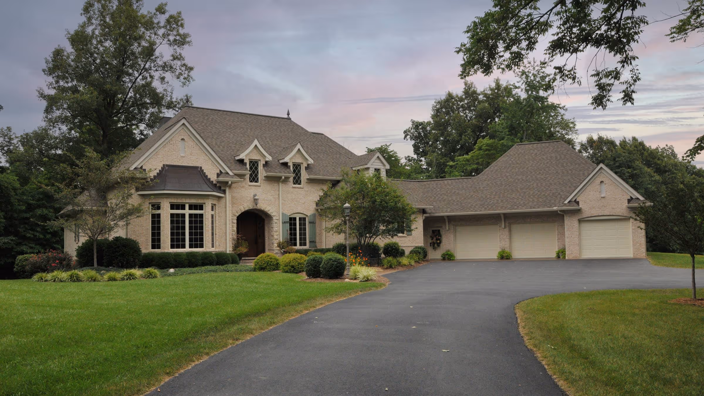 Large French Eclectic style house with beige brick exterior, three-car garage, curved driveway, and landscaped front lawn.