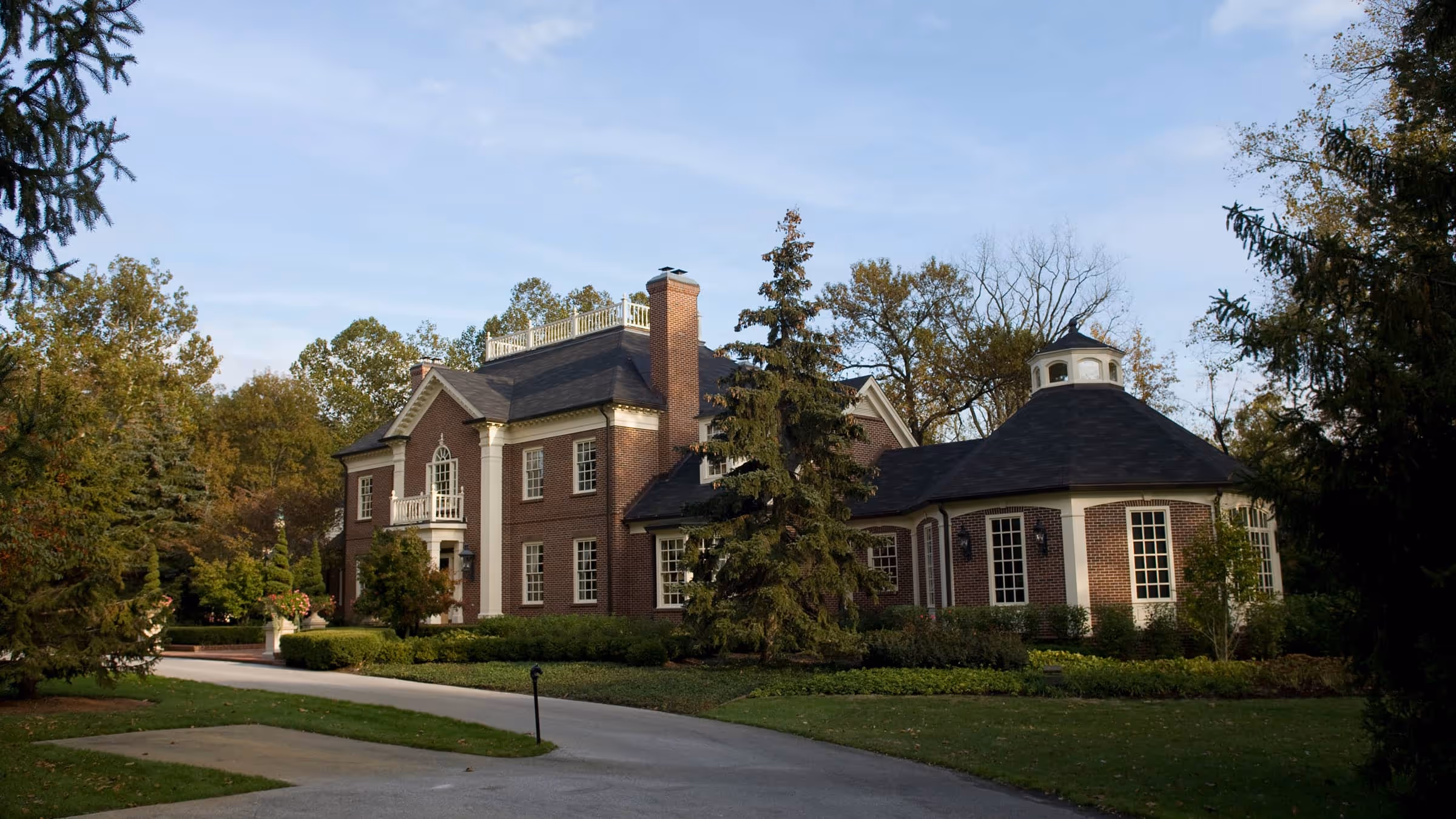 Large brick Georgian style house with multiple windows, a tall chimney, and a circular turret surrounded by trees and garden.
