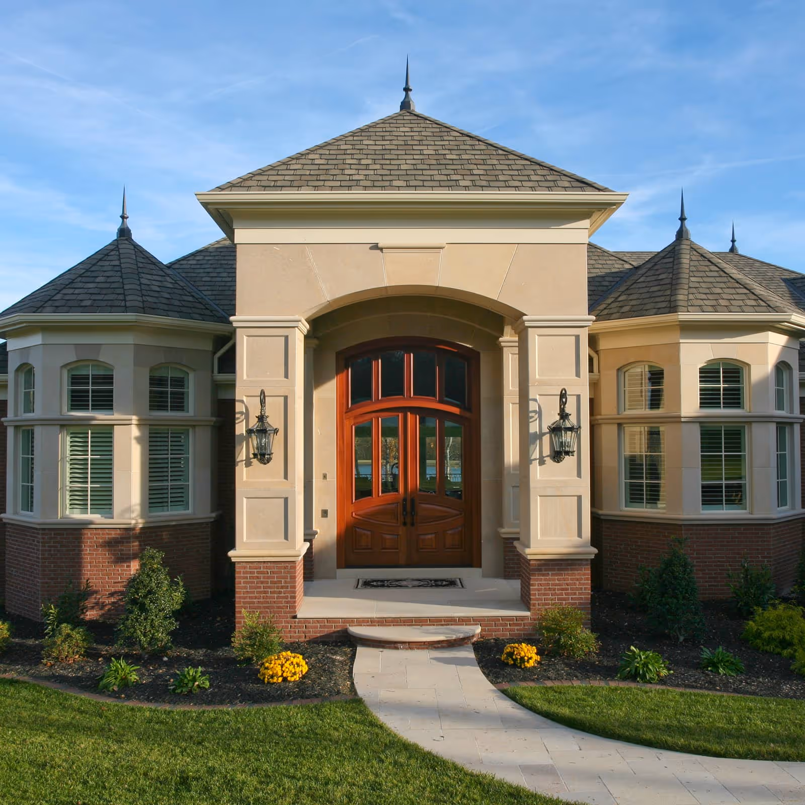 Elegant house entrance with arched wooden double doors, twin lantern sconces, and symmetrical bay windows.