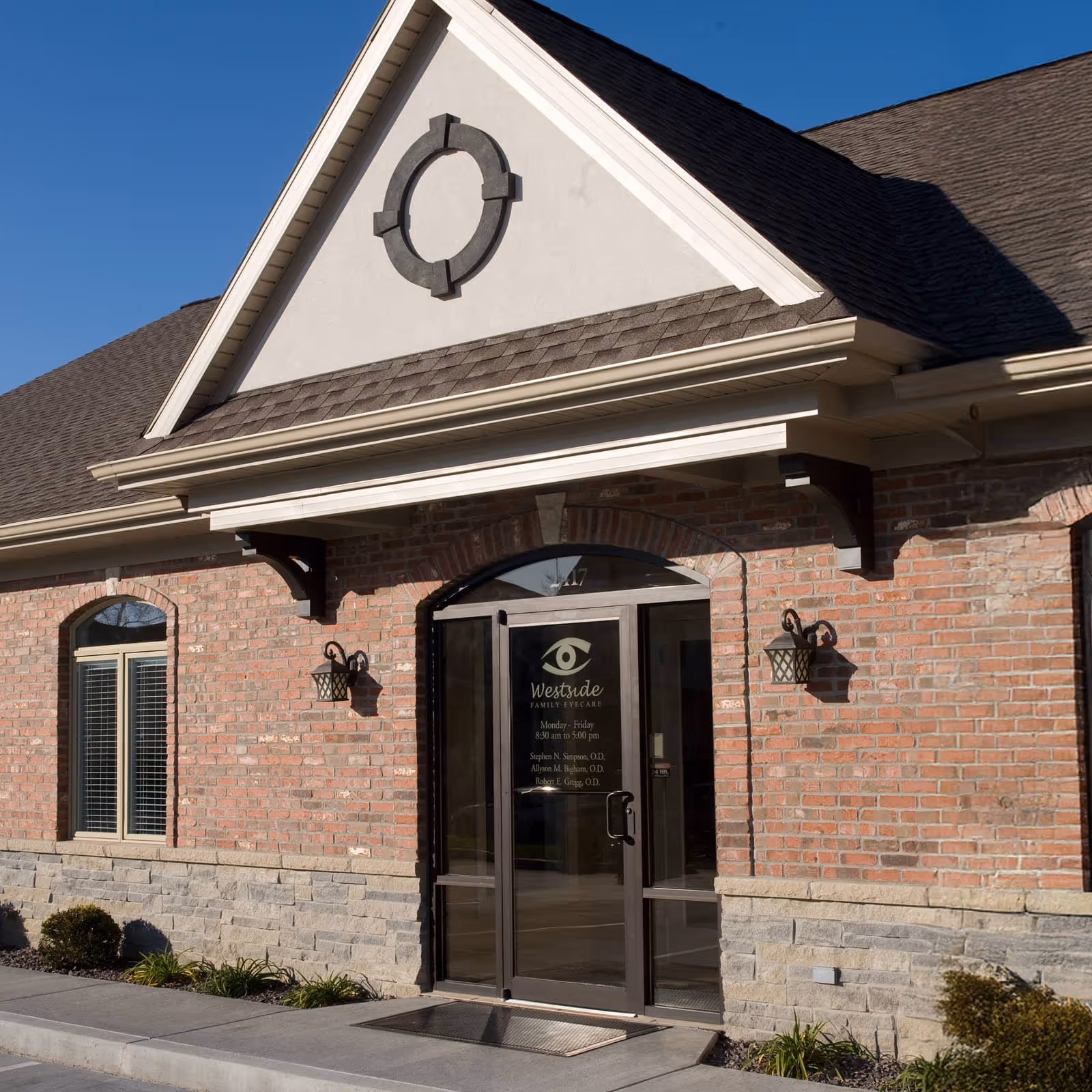 Entrance to a brick and stone clinic with glass door displaying Westside Family Eyecare logo and hours.