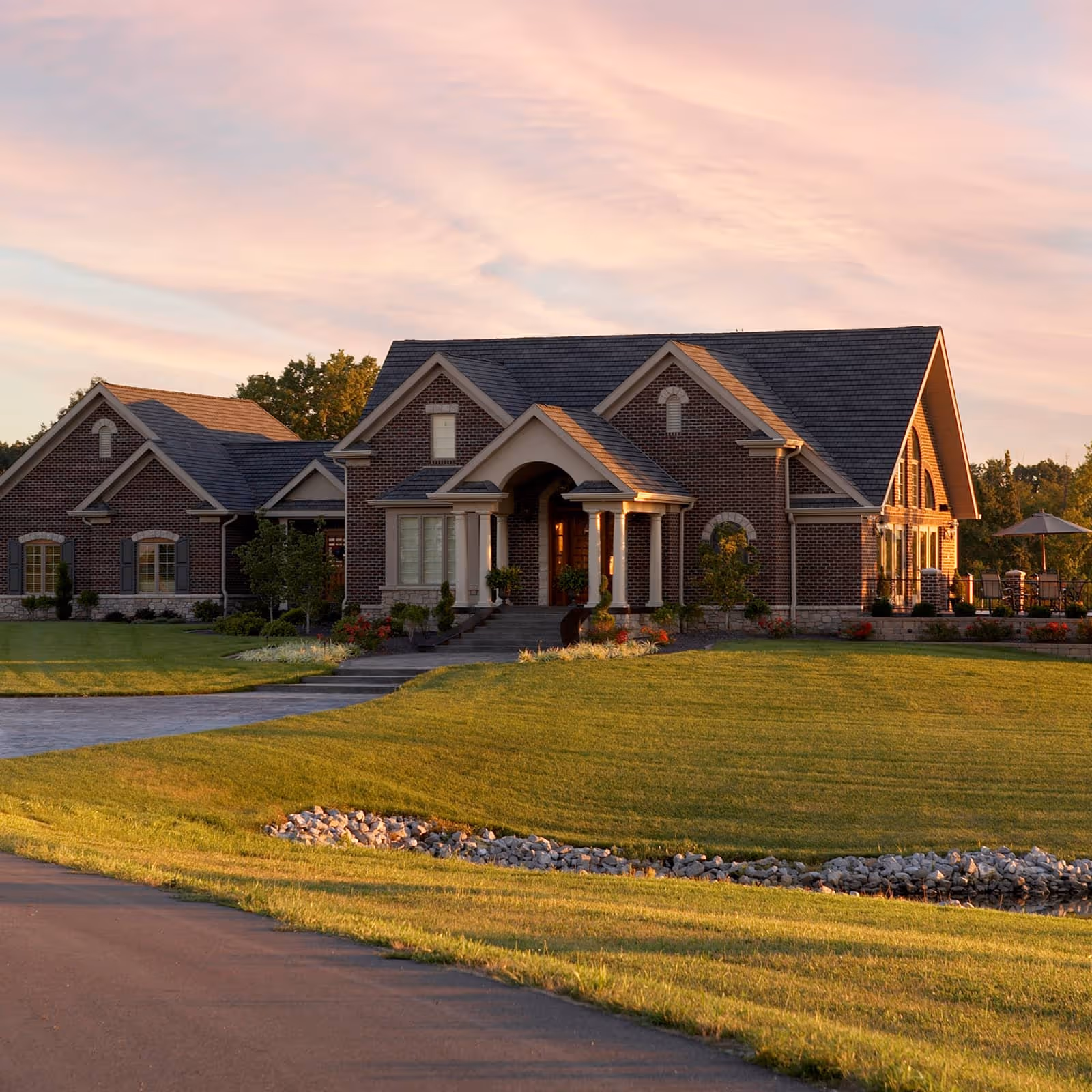 Large brick house with a manicured lawn and stone pathway under a pink sunset sky.