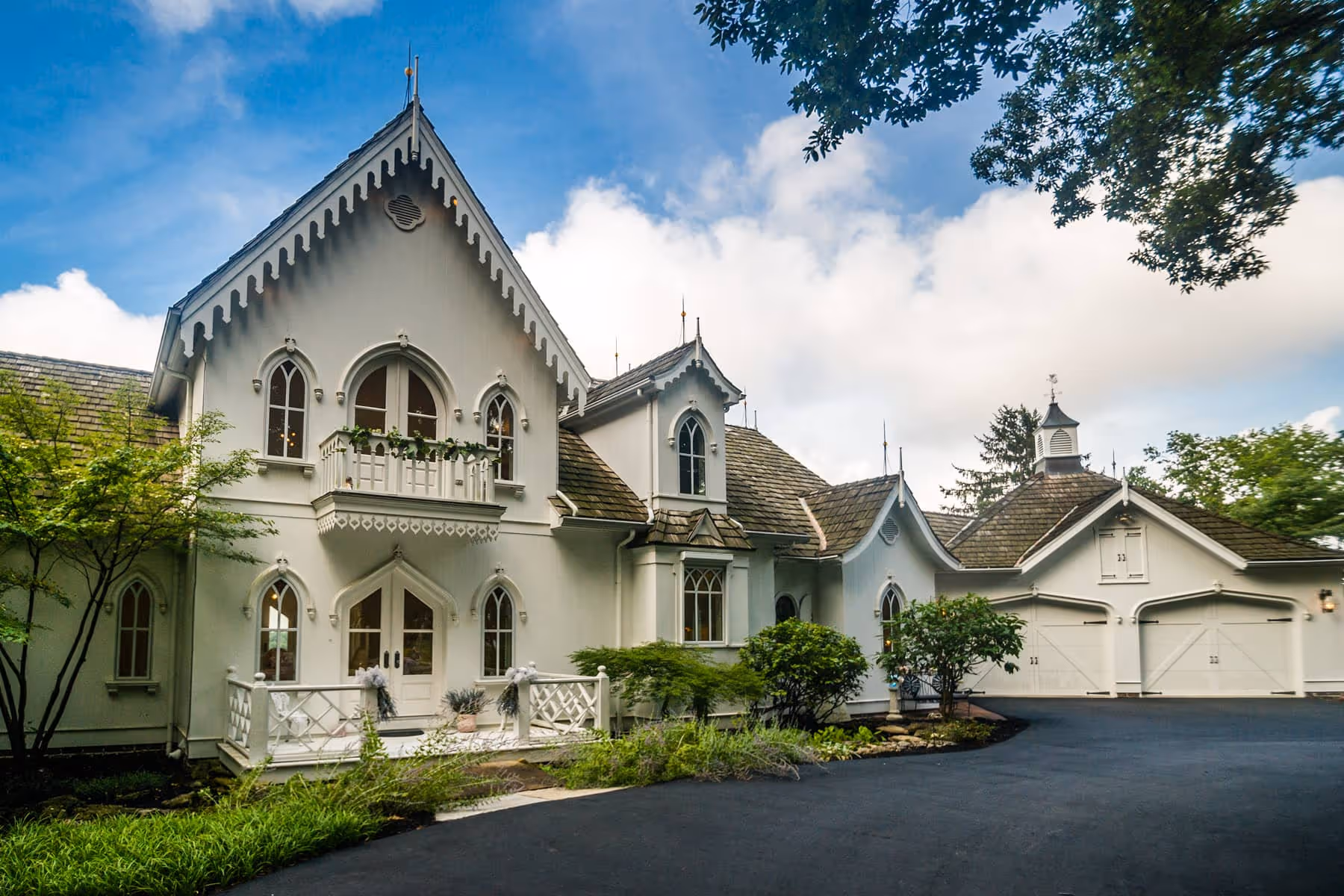 White Gothic Revival style house with steep gabled roof, pointed arch windows, and a three-car garage under a blue sky.