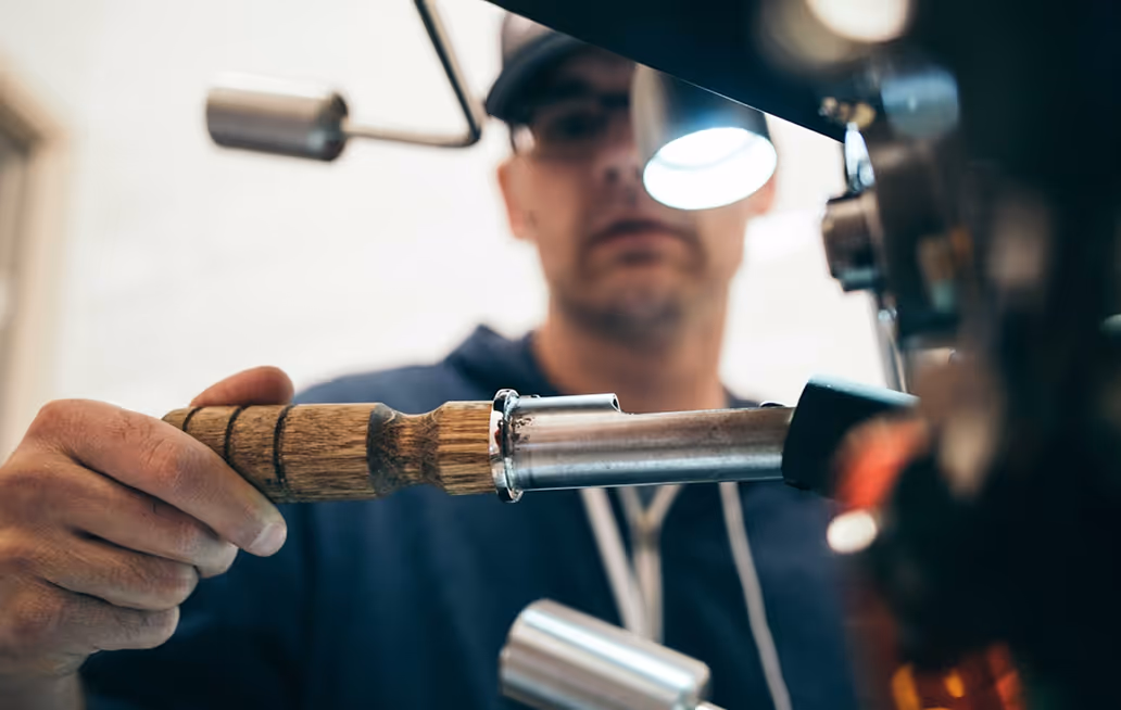 Man operating a coffee machine by holding a wooden-handled portafilter.