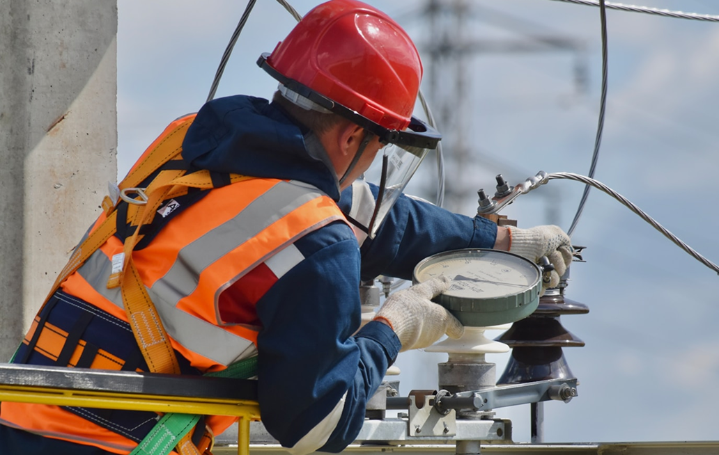 Electric utility worker wearing safety gear and helmet repairs power lines on a utility pole.
