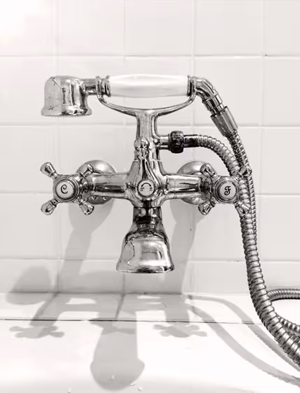 Chrome bathtub faucet with a handheld shower head against white tile