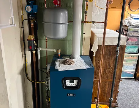 Blue Dunkirk boiler unit with attached pipes and an expansion tank in a basement room.