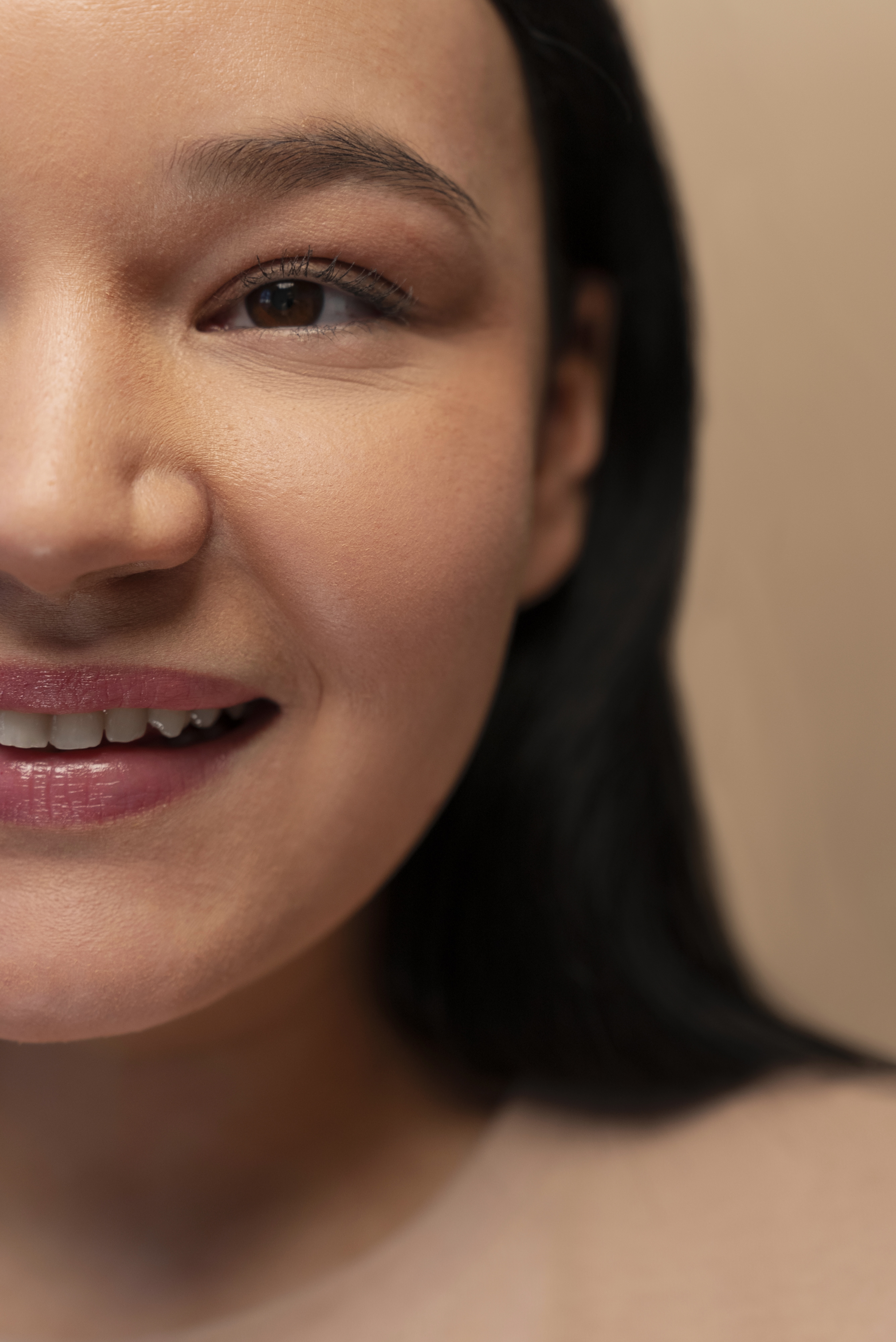 Close-up of the left side of a smiling woman's face with smooth skin and dark hair.