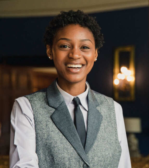 Smiling hospitality professional wearing a grey waistcoat, white shirt, and black tie, representing the efficiency Onso brings to hotels, restaurants, and venue supply chain management. Image emphasizes service and operations support.
