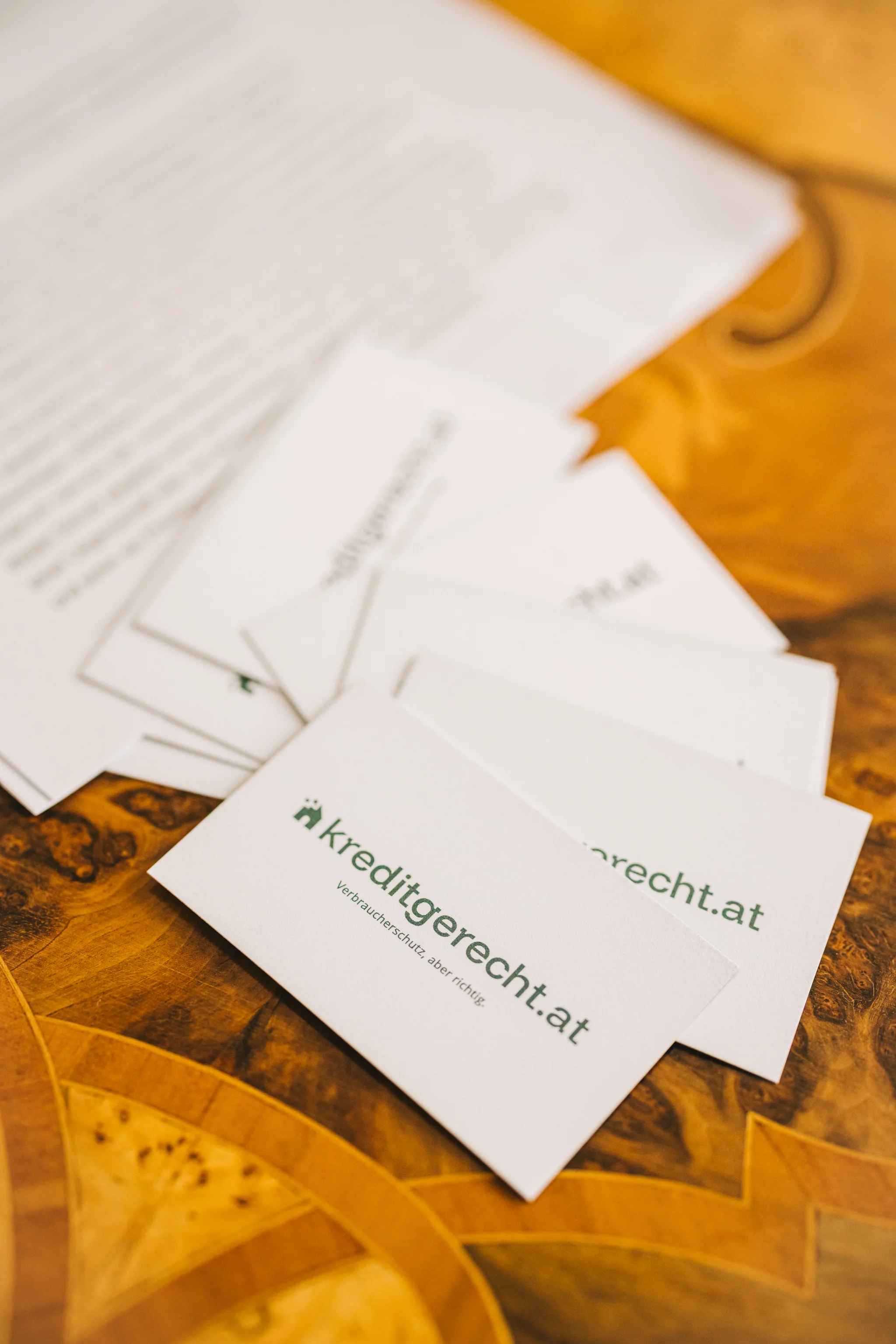 Stack of kreditgerecht.at business cards on a wooden table with a blurred document in the background.