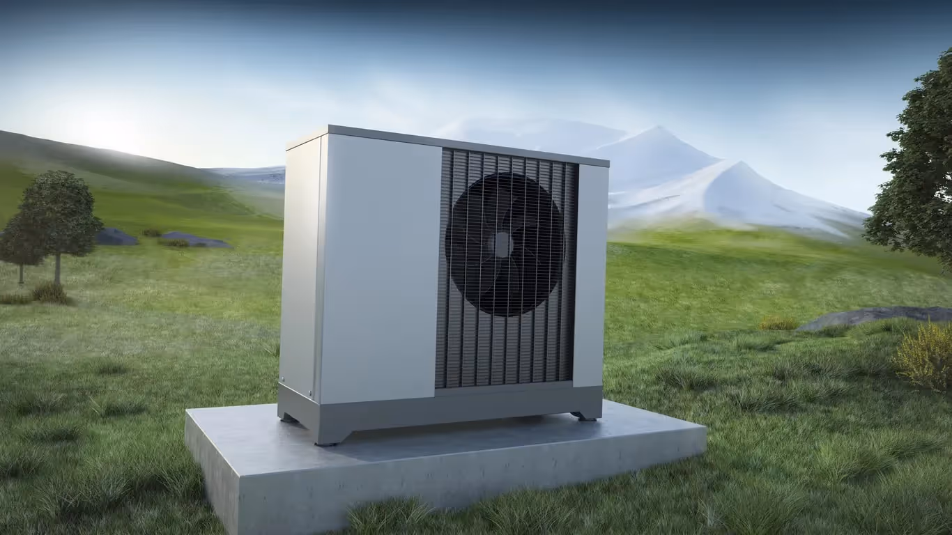 A heat pump unit sits on a concrete slab in a lush, green field with rolling hills and a snow-capped mountain in the background.