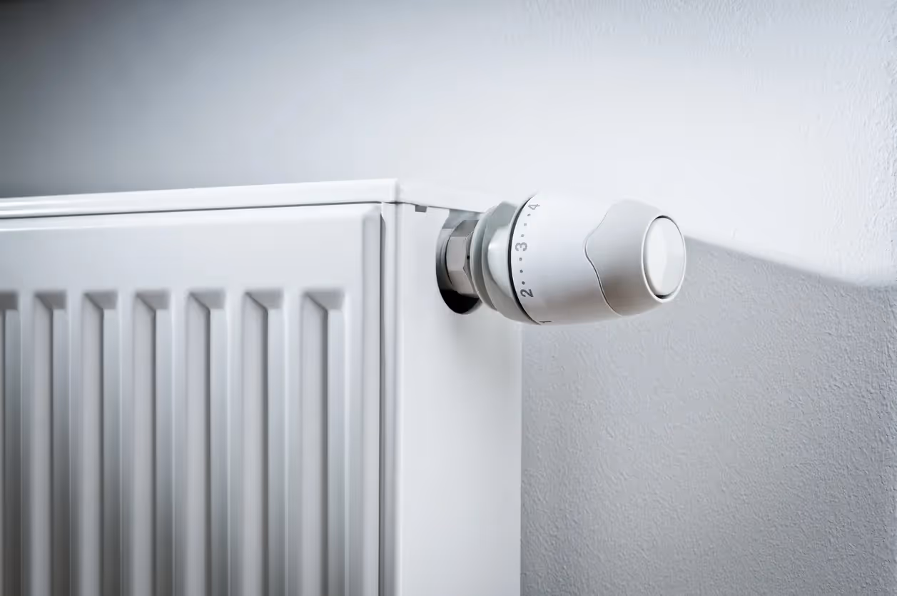 A close-up of a modern white thermostatic radiator valve on a panel radiator