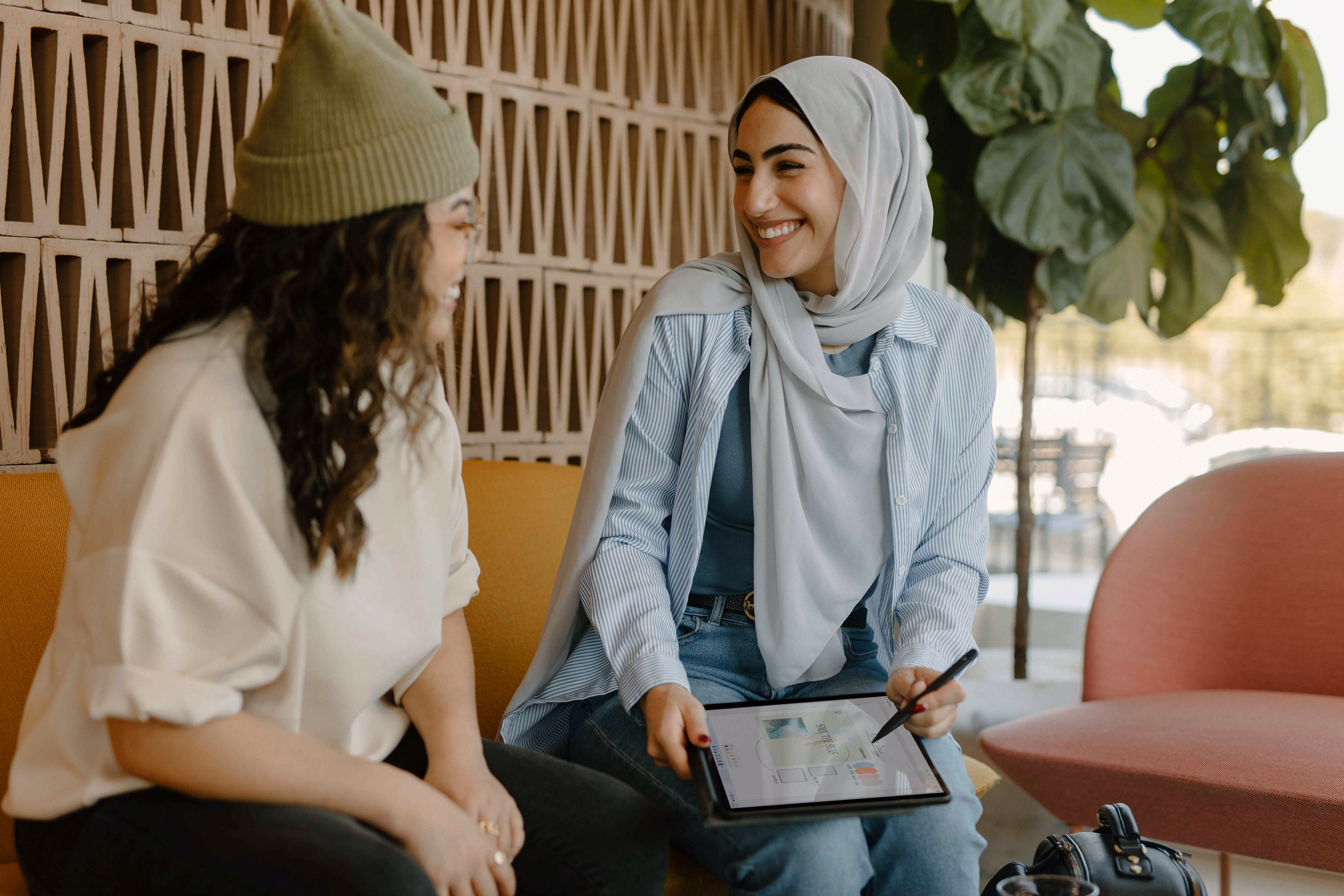 Two women sitting and smiling, one showing digital charts on a tablet to the other.