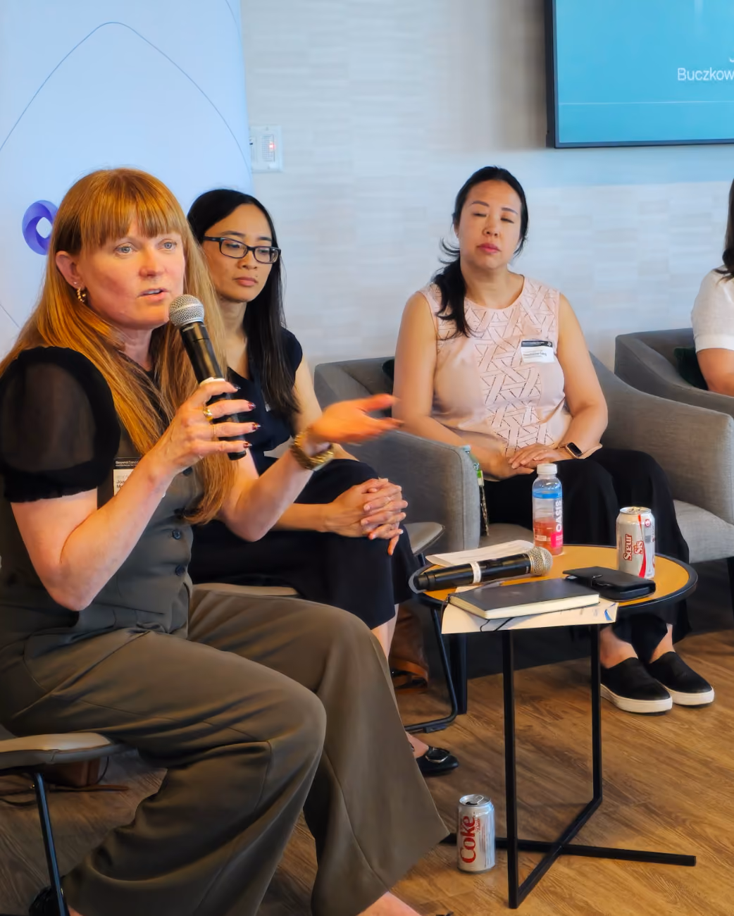 Woman with microphone speaking while two others listen during a panel discussion in a room.