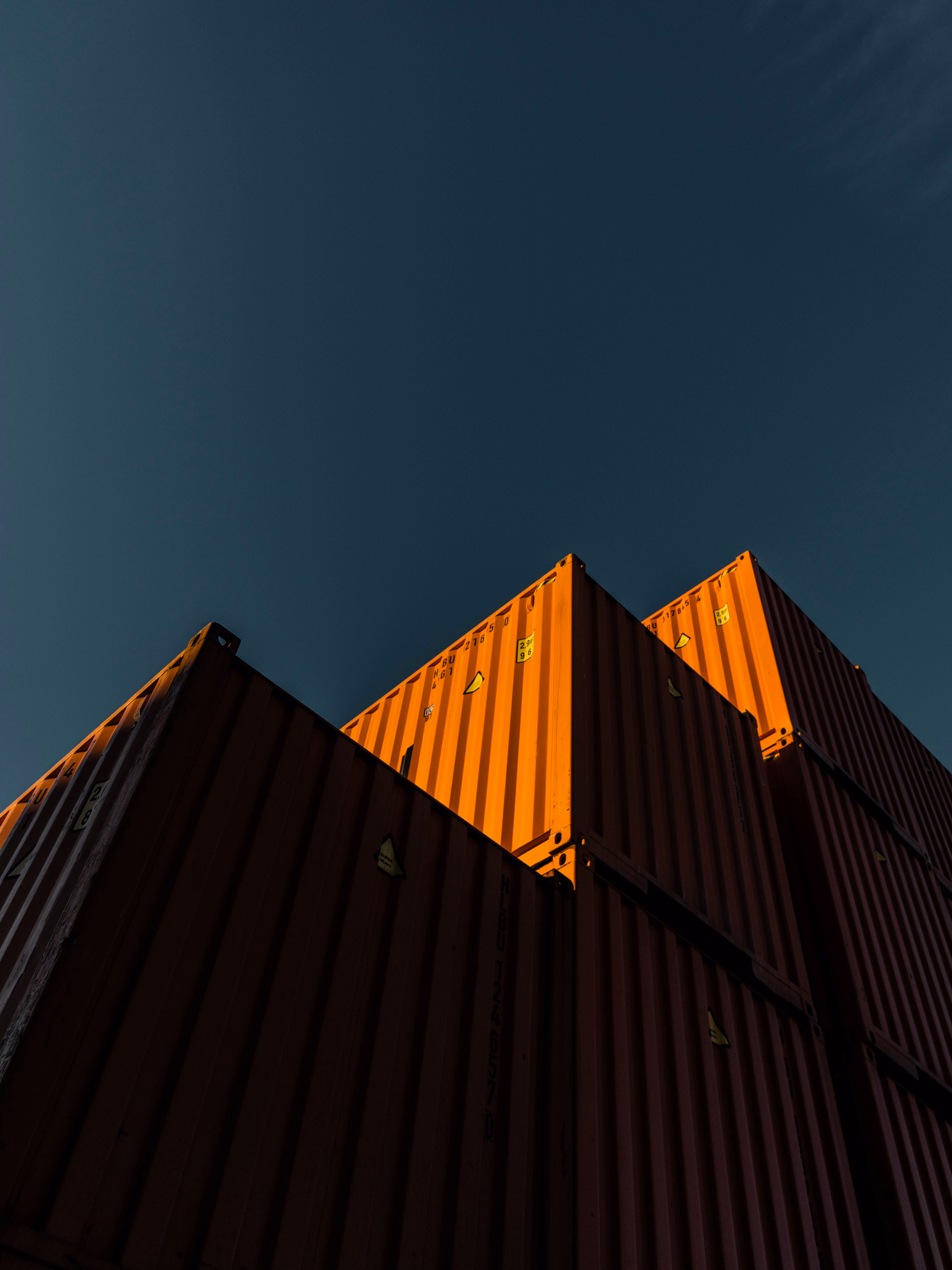 Stack of orange shipping containers under a deep blue, cloudless sky.