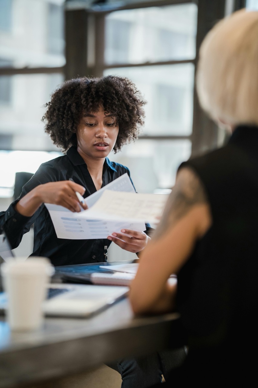 Two people work across from each other at a desk, examining and sharing paperwork