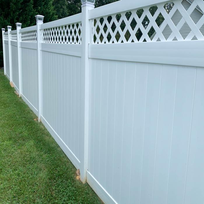 White vinyl privacy fence with lattice design on top along a grassy area.