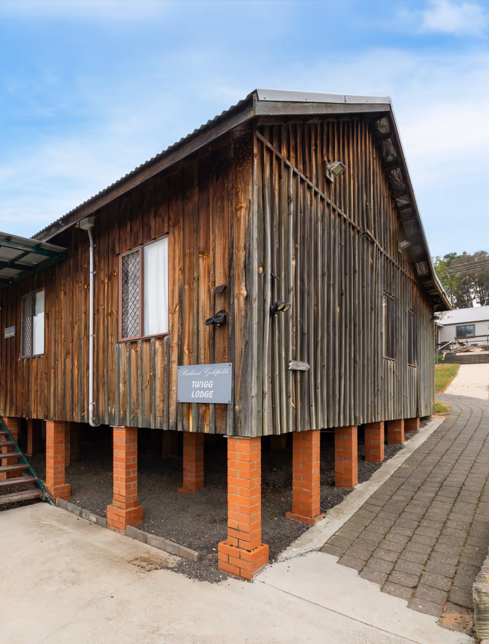 Elevated wooden lodge with vertical planks supported by brick pillars under a blue sky.