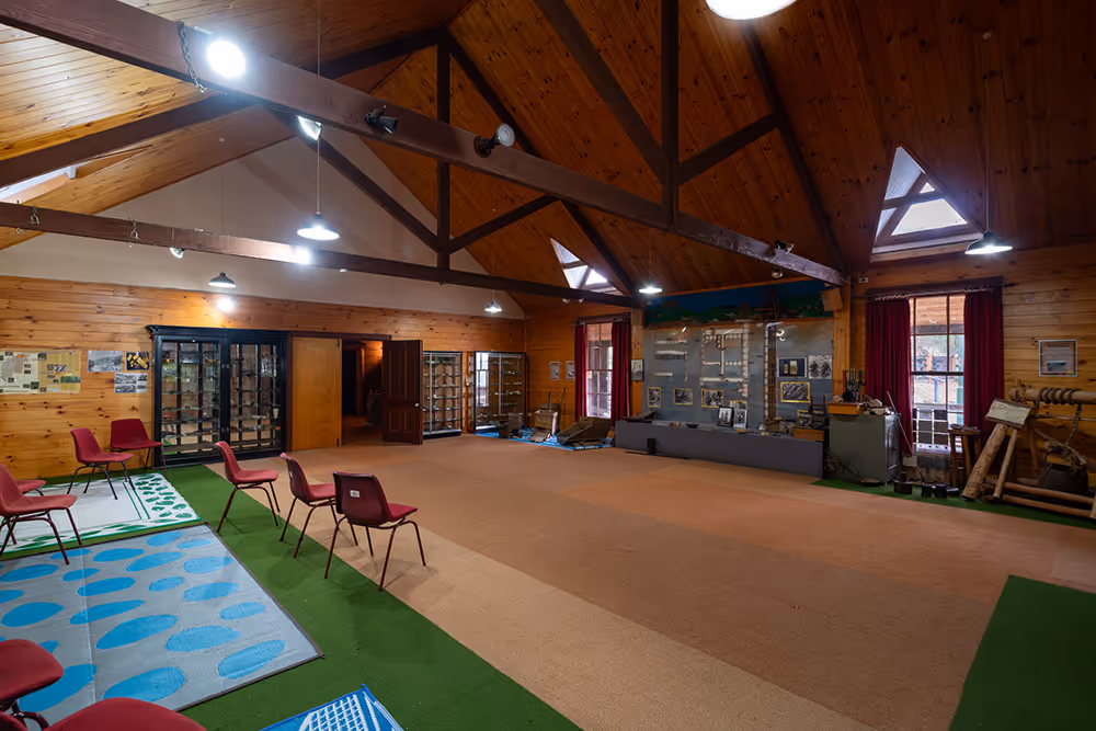 Spacious wooden interior room with red chairs arranged along green and blue mats and display cases along the walls.