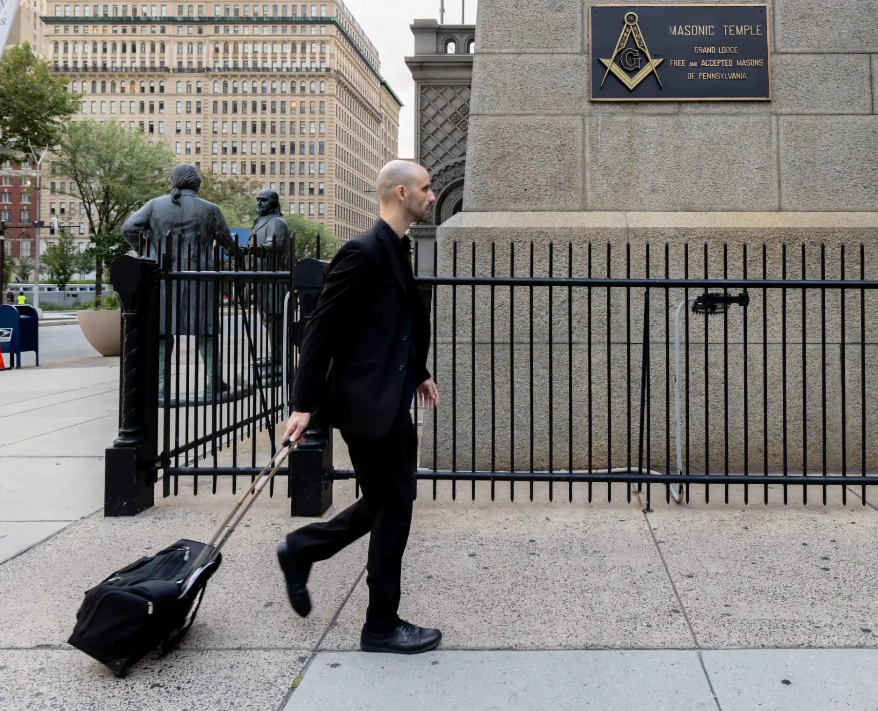 Magician Jesse Dameron walking with a rolling case past the Masonic Temple Grand Lodge plaque at One North Broad