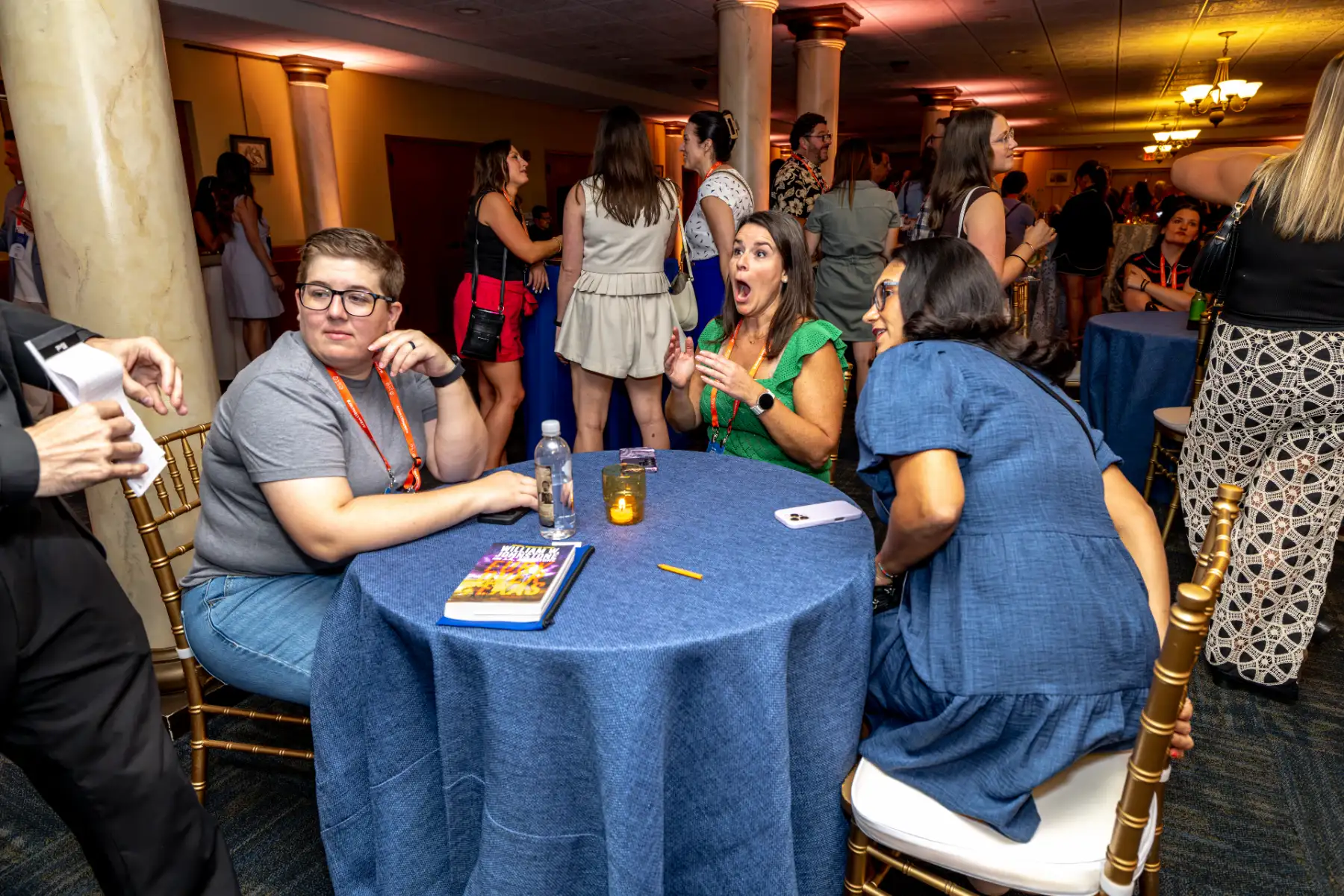 A seated guest gasps as mentalist and magician Jesse Dameron performs at a table in the crowded Wanamaker Ballroom