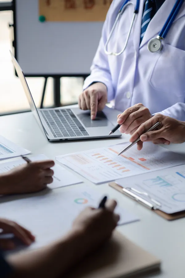 Medical professionals reviewing charts and data on a laptop and printed papers during a meeting.
