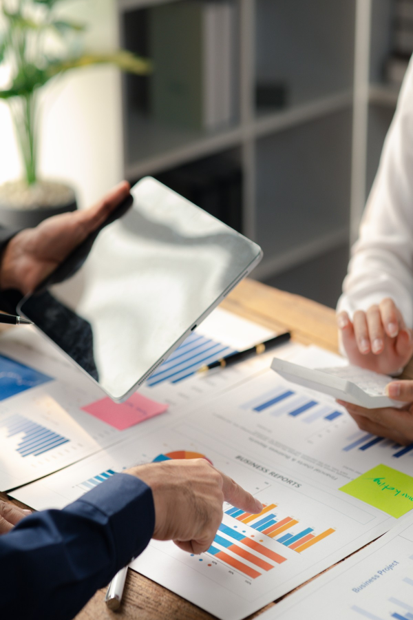 Hands of business people pointing and discussing charts and graphs on printed reports at a desk.